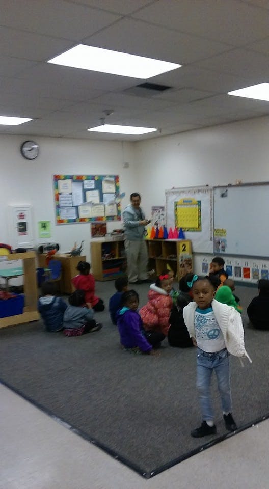Person standing in front of children sitting on a rug in a classroom