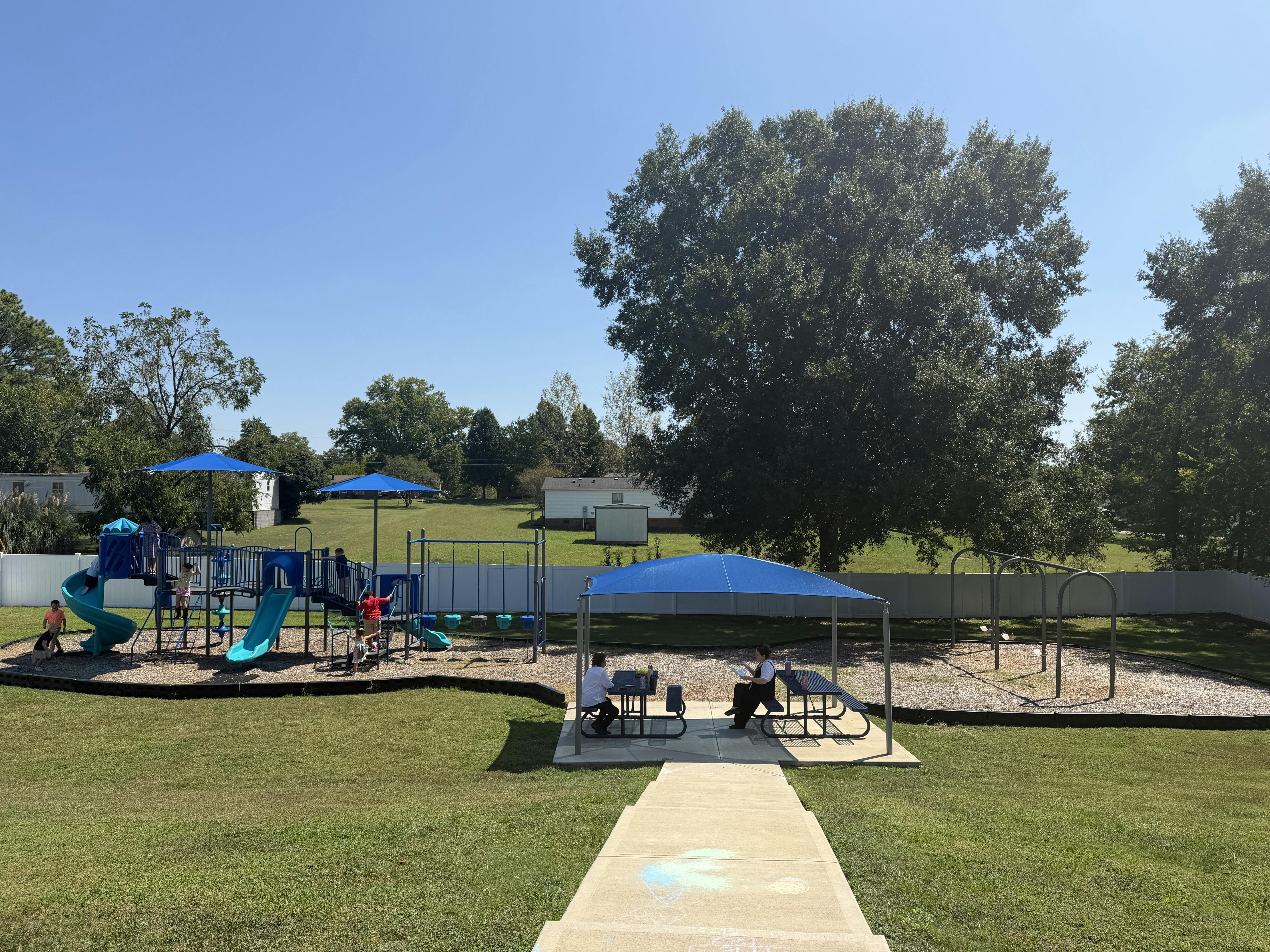 People using a playground and picnic tables under a shade canopy
