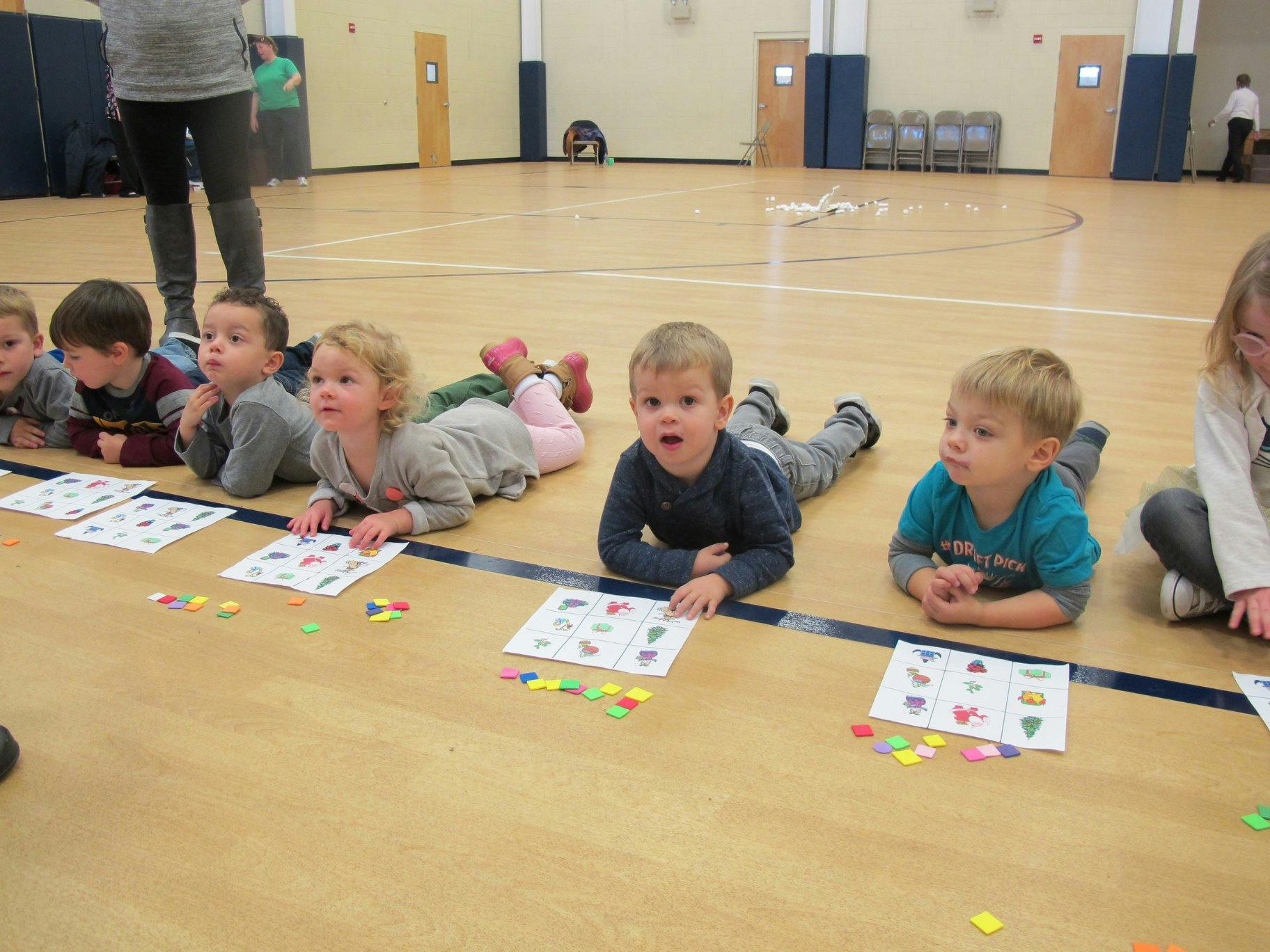 Children lying on a gym floor with papers and small colorful pieces