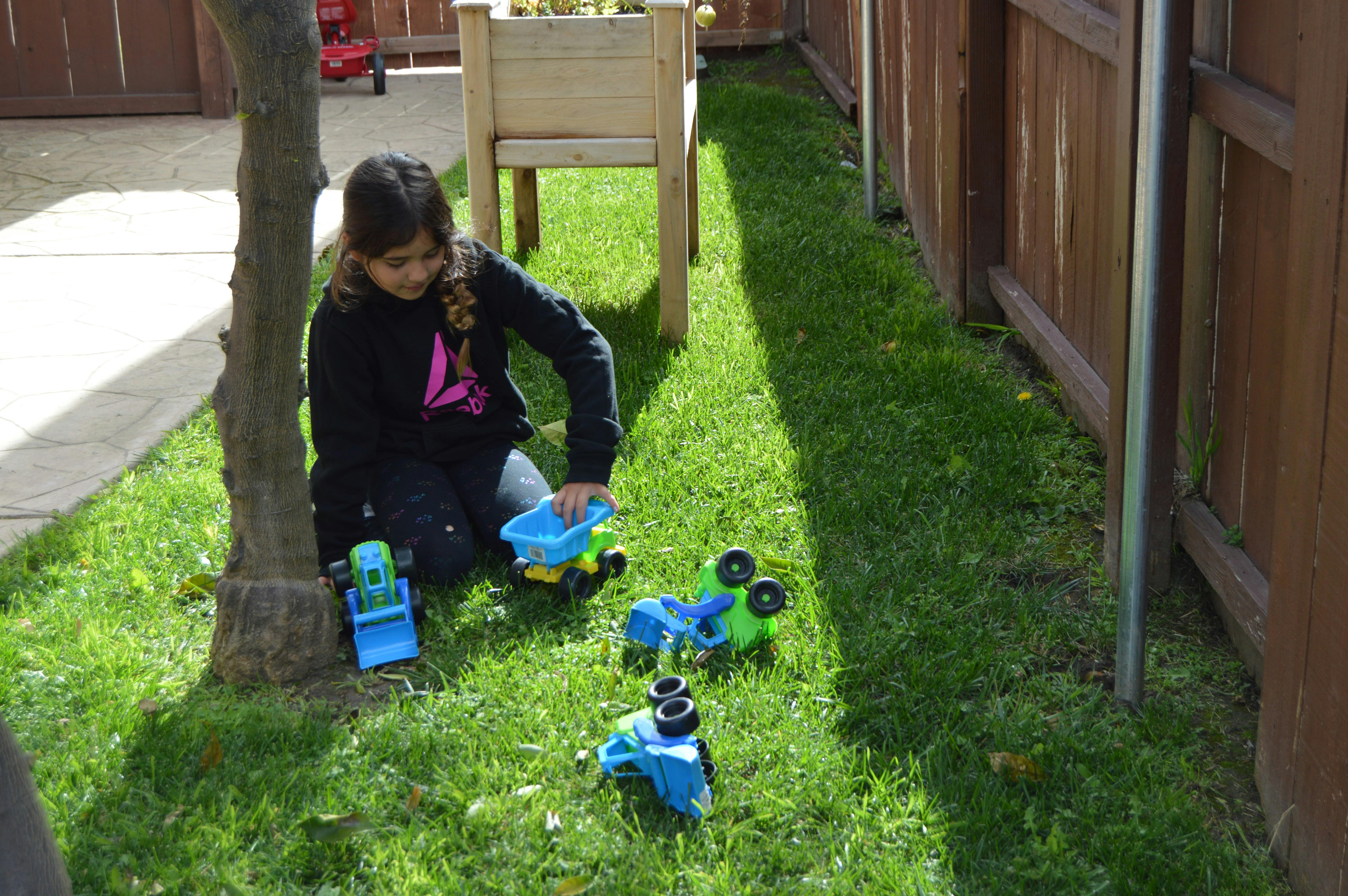 Child kneeling on grass playing with toy trucks