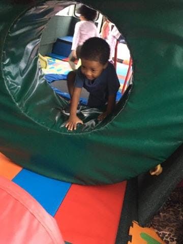 Child crawling through a green tunnel in an indoor play area
