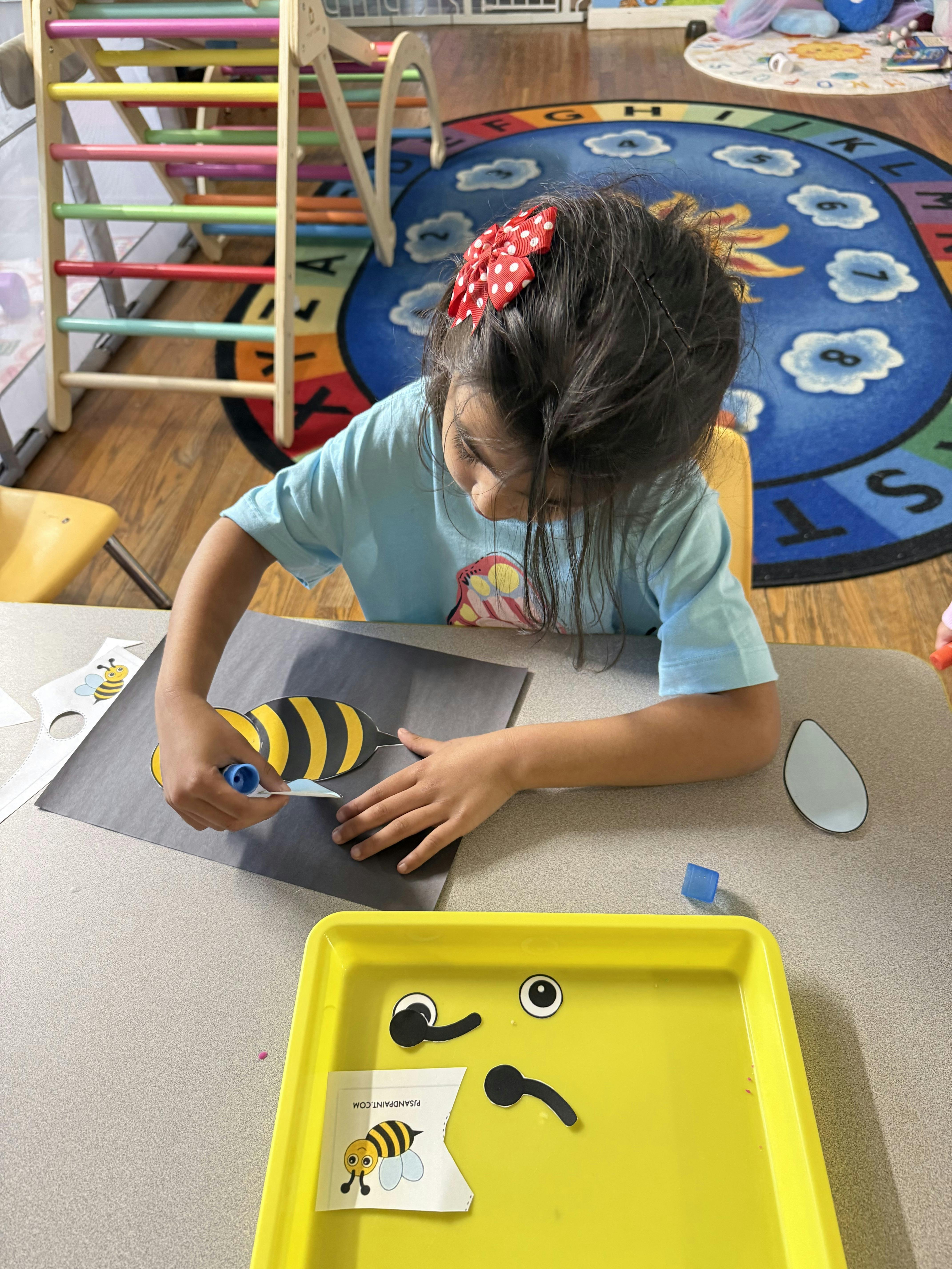 Child gluing paper bee pieces at a table