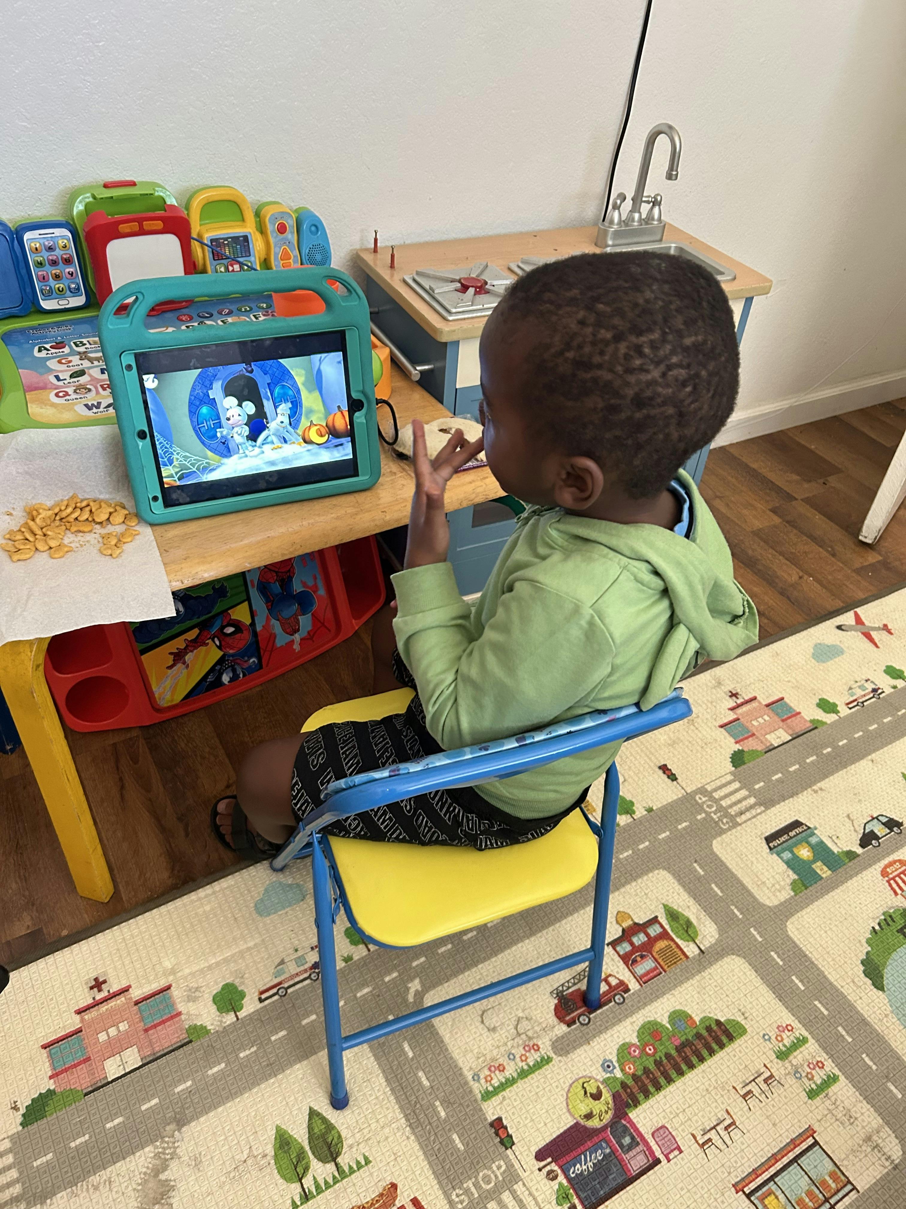 Child watching a tablet while sitting on a yellow and blue chair
