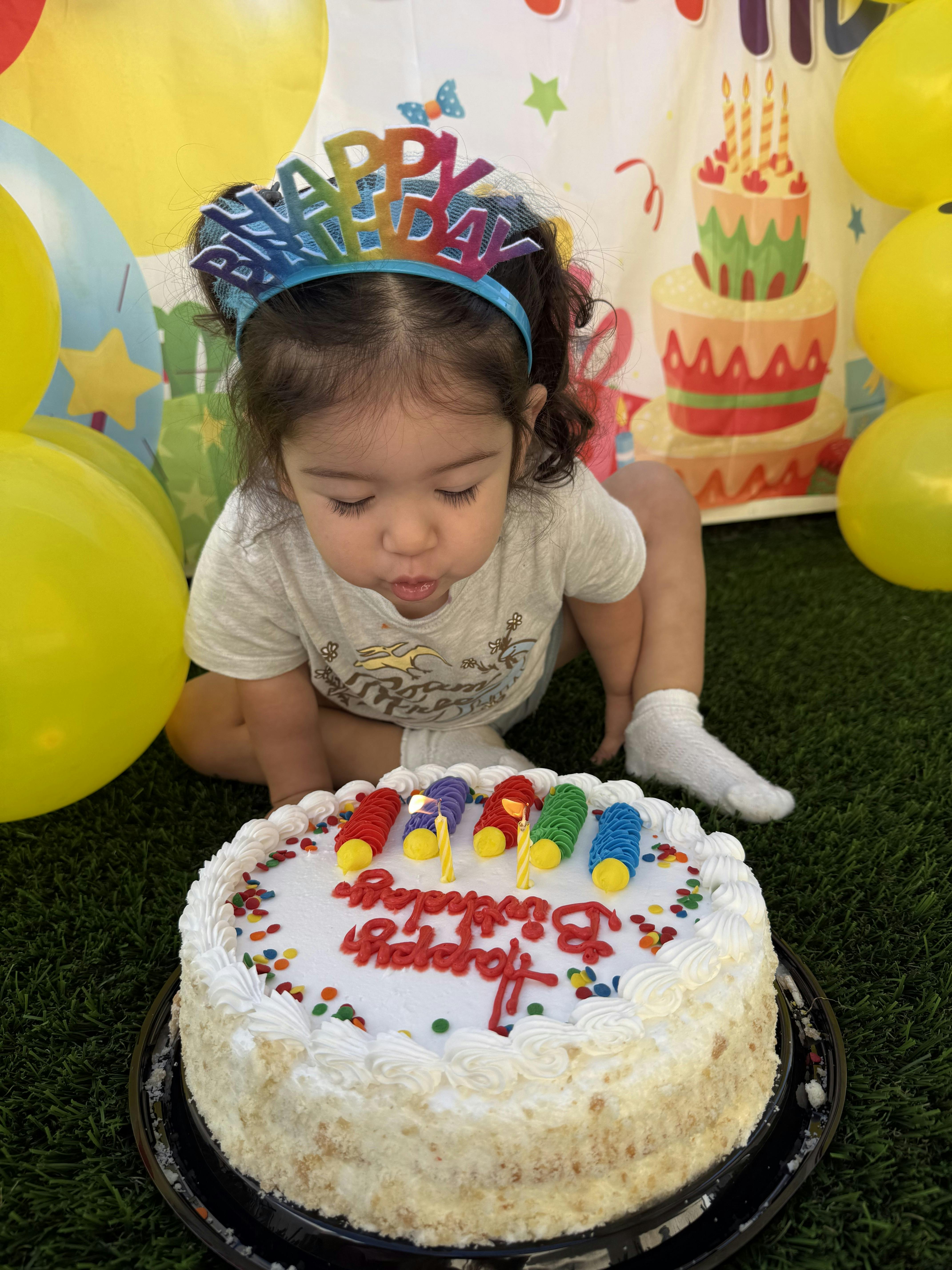 Child wearing a birthday headband blowing out candles on a birthday cake