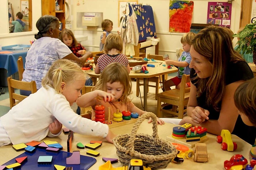 Adults and children playing with toys at tables in a classroom
