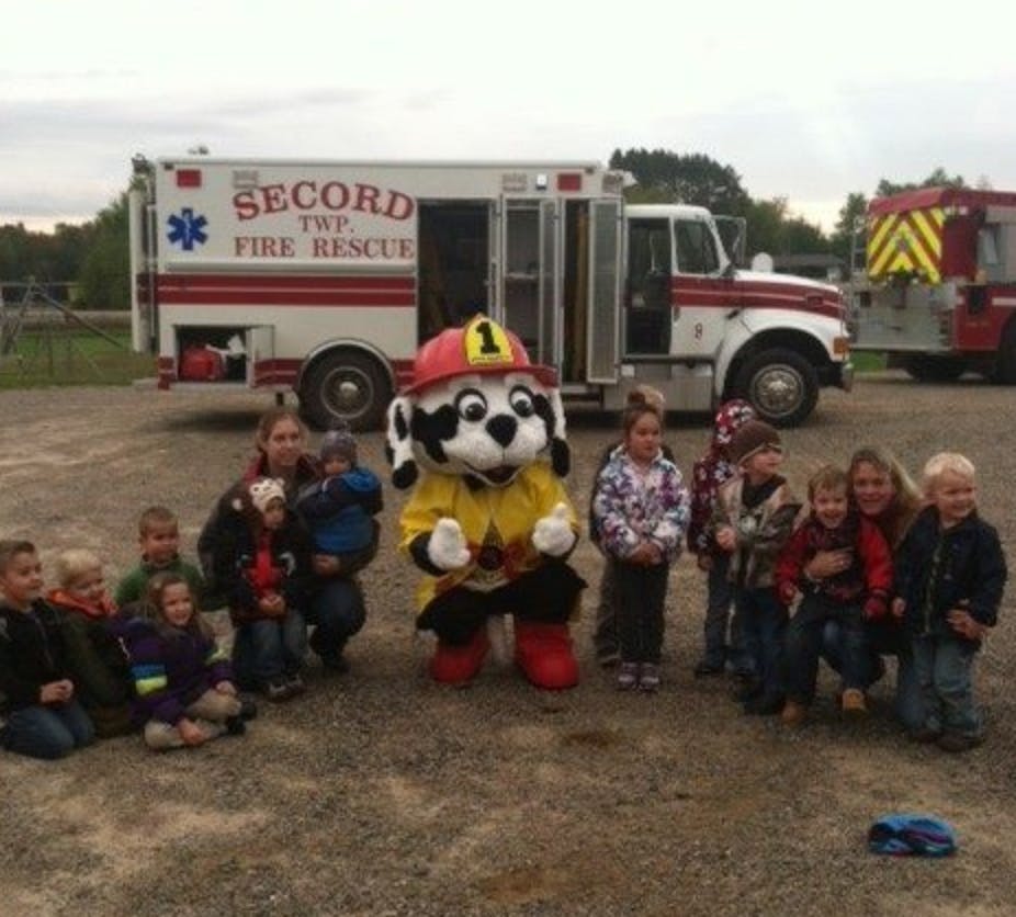 Mascot in firefighter costume with adults and children in front of an ambulance