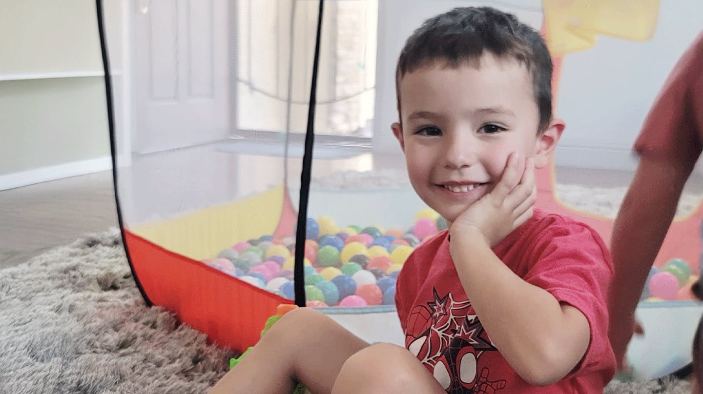 Child in red shirt with hand on cheek next to a ball pit