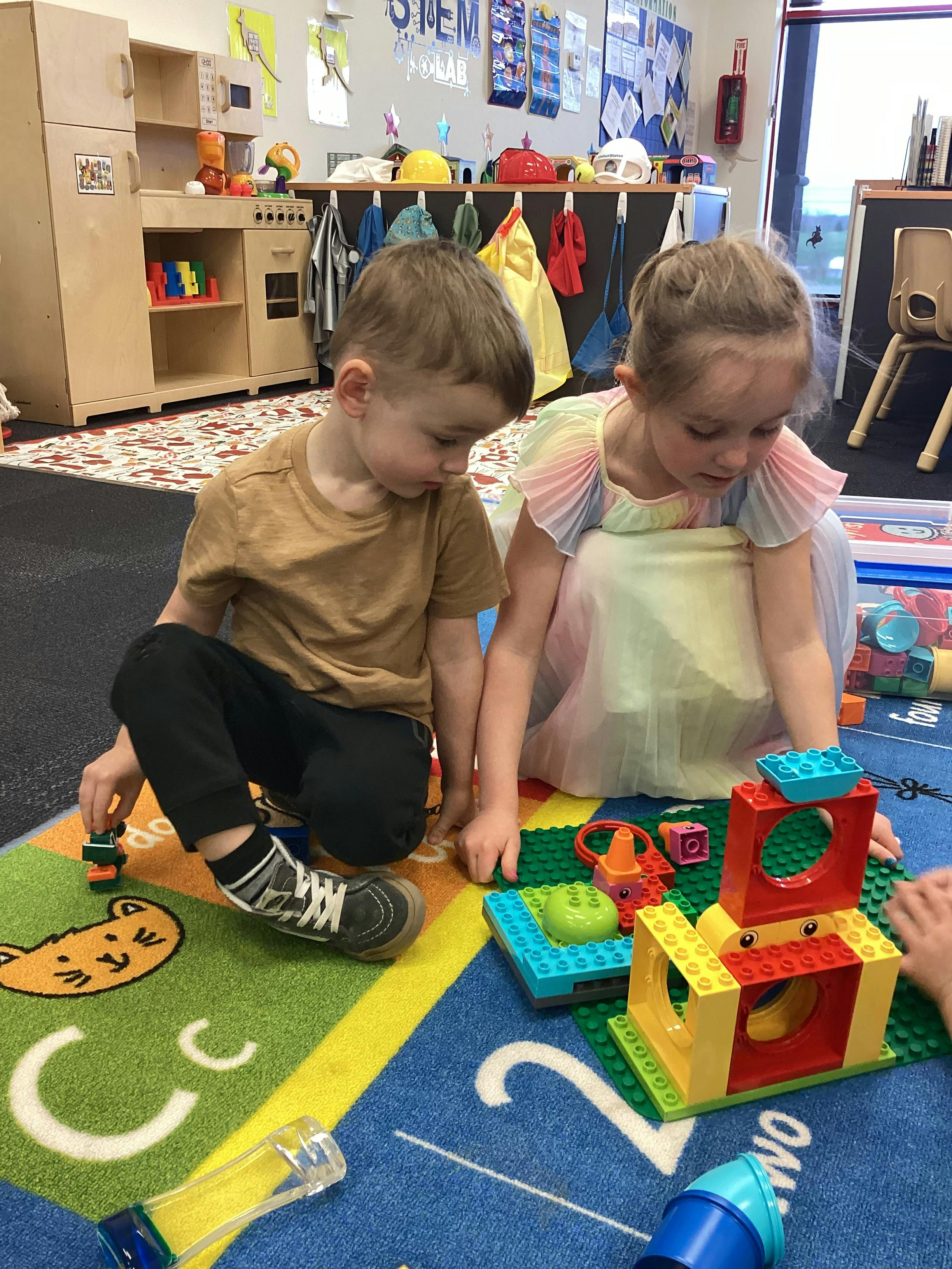 Two children playing with building blocks on a colorful rug in a classroom