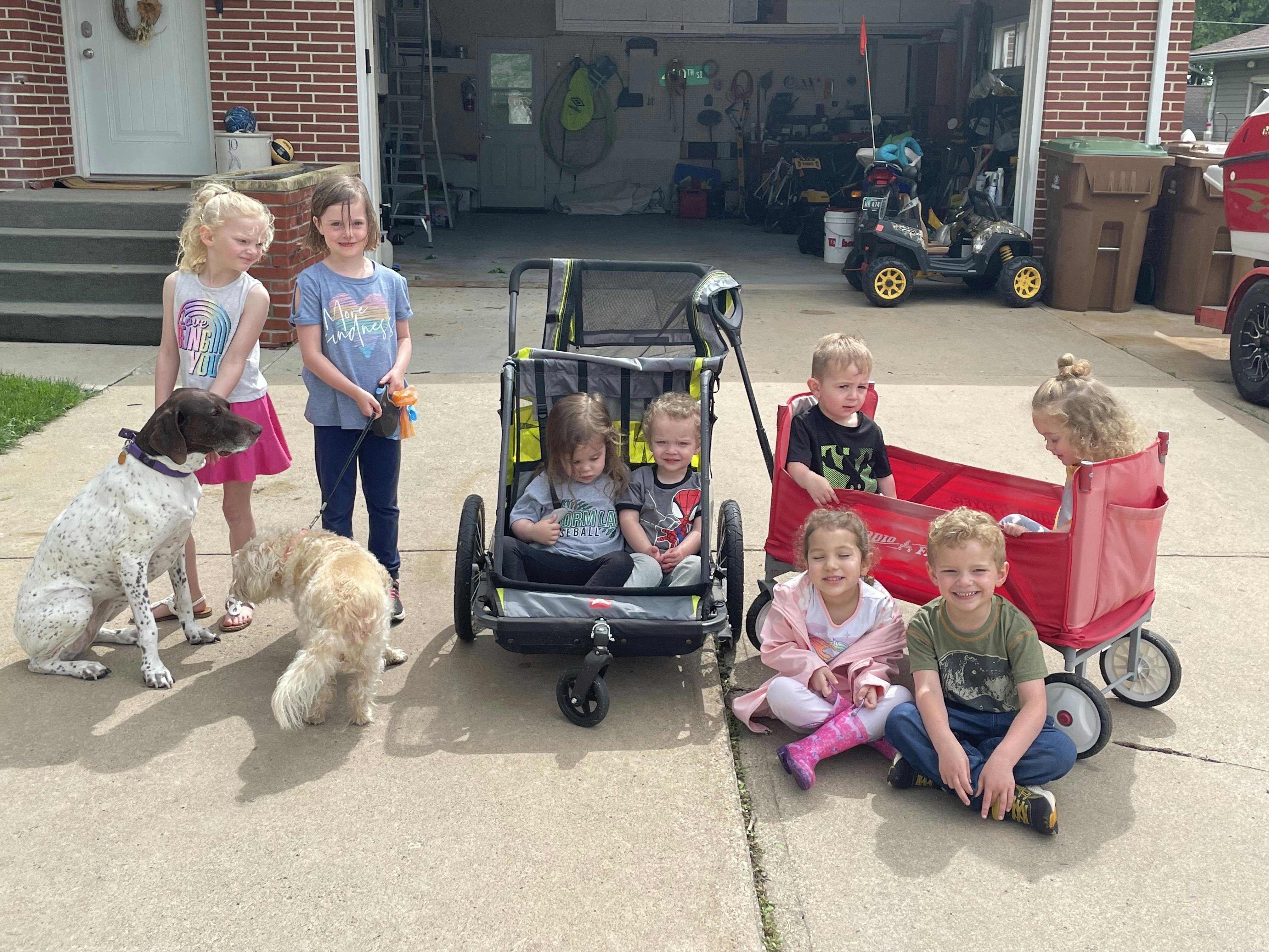 Group of children and two dogs on a driveway with two wagons