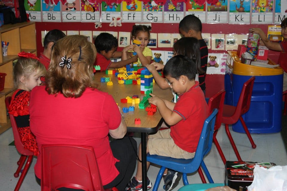 Adult and children playing with colorful building blocks at a table in a classroom