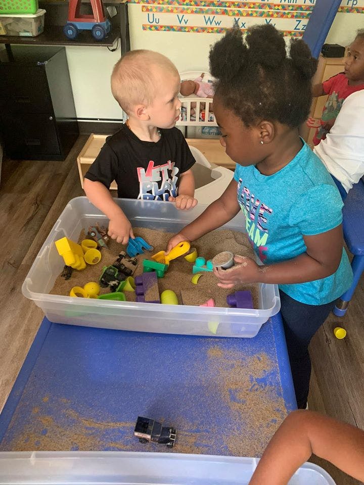 Two children playing with sand and toys in a plastic bin