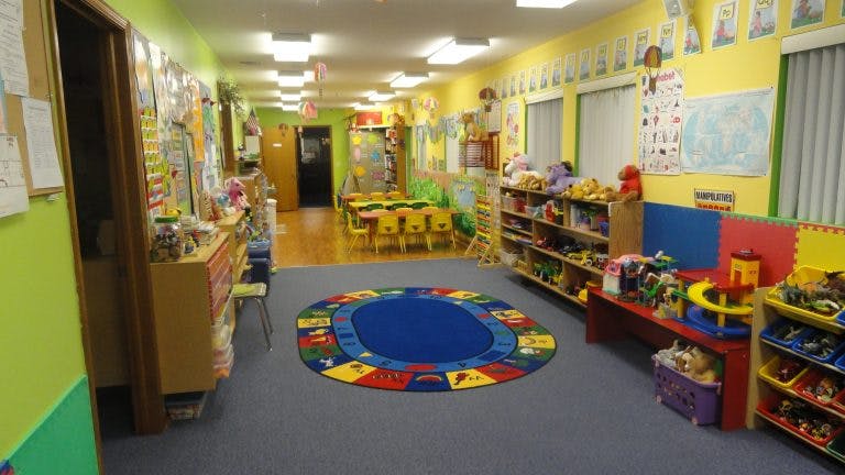 Playroom with a colorful rug, shelves of toys, and small tables and chairs