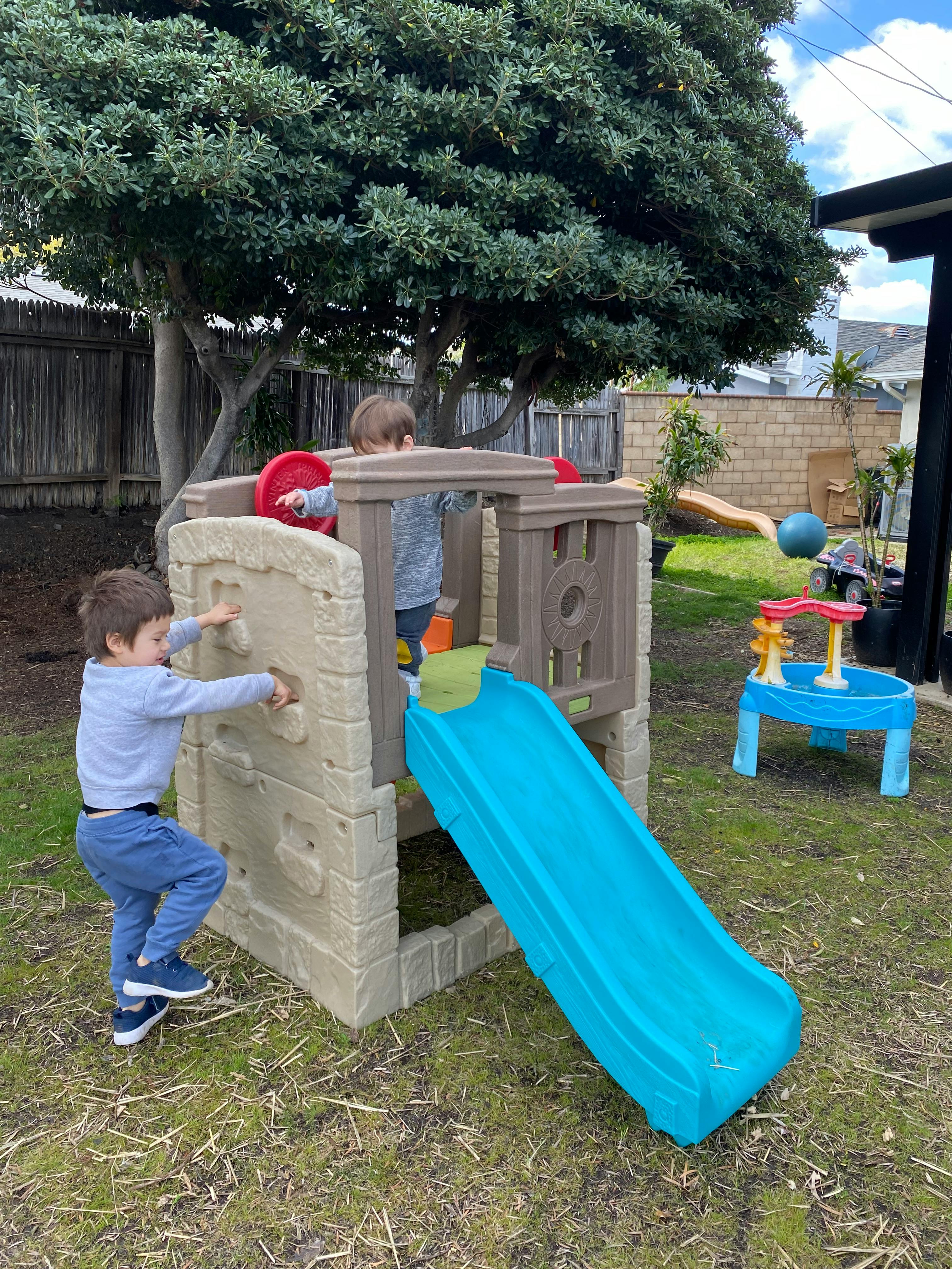 Two children playing on a small outdoor playset with a slide