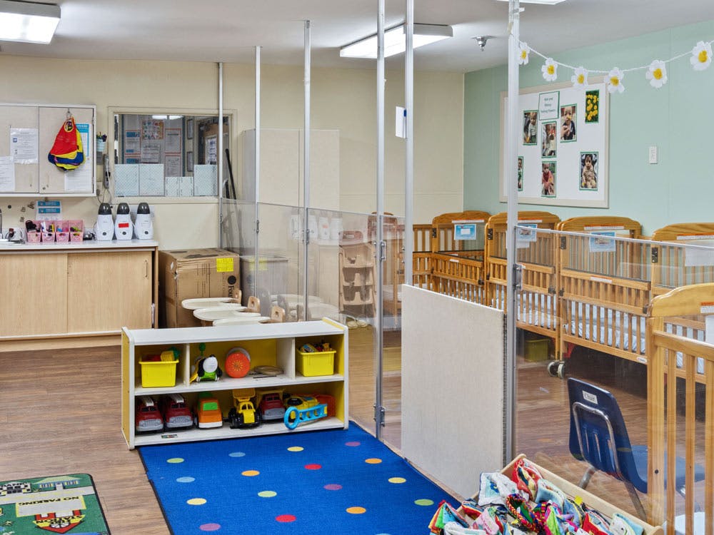cribs in a daycare room with a toy shelf and colorful rug