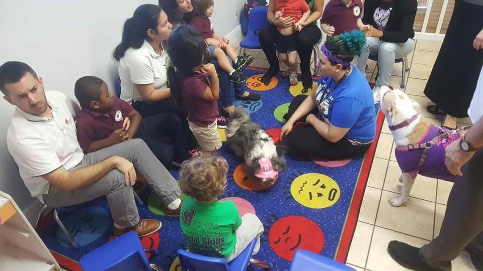 People and children sitting on a rug with a dog and a person in a blue shirt