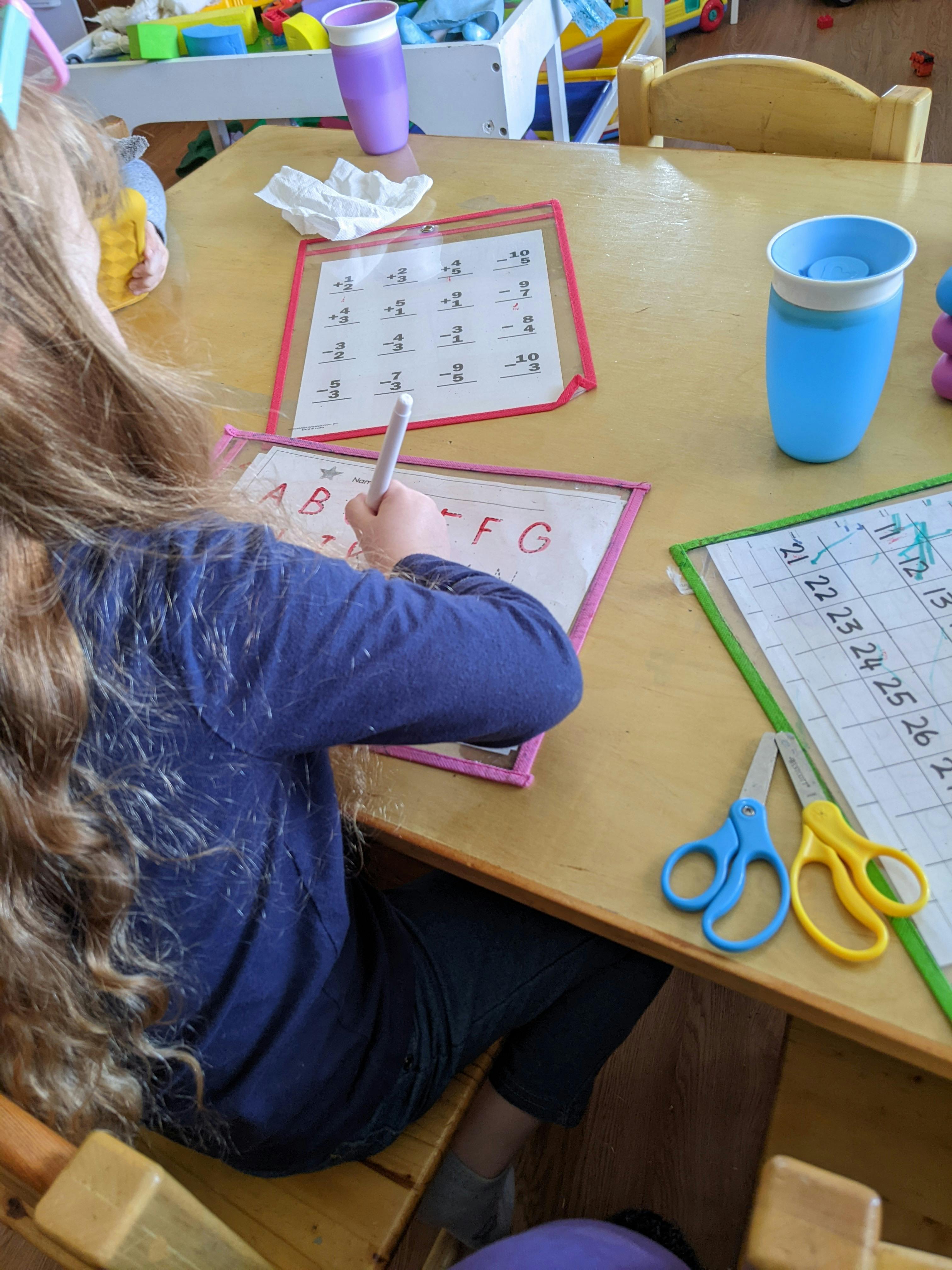 Child writing letters on a worksheet at a table