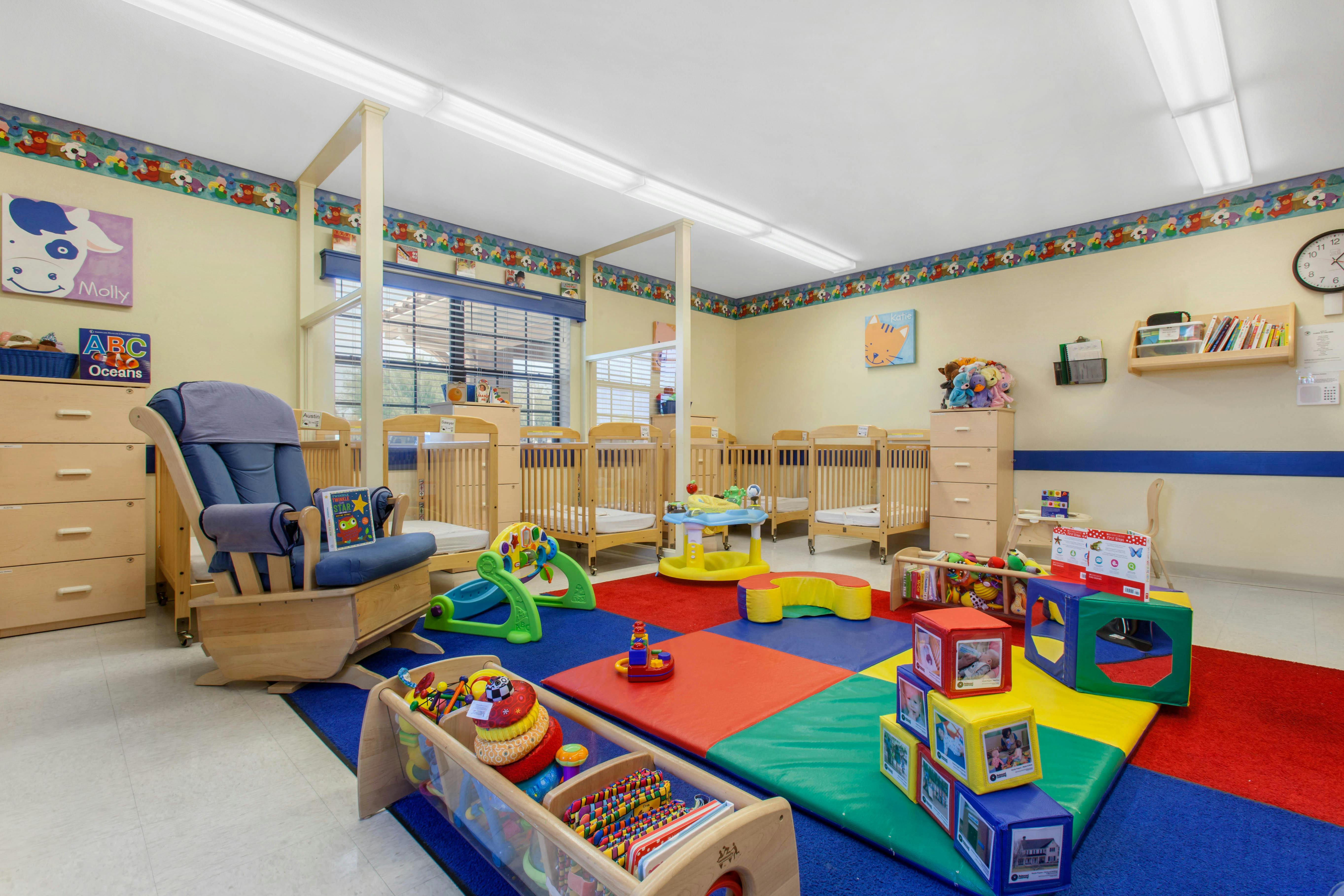 Classroom with multiple cribs, a rocking chair, colorful mats, and toys