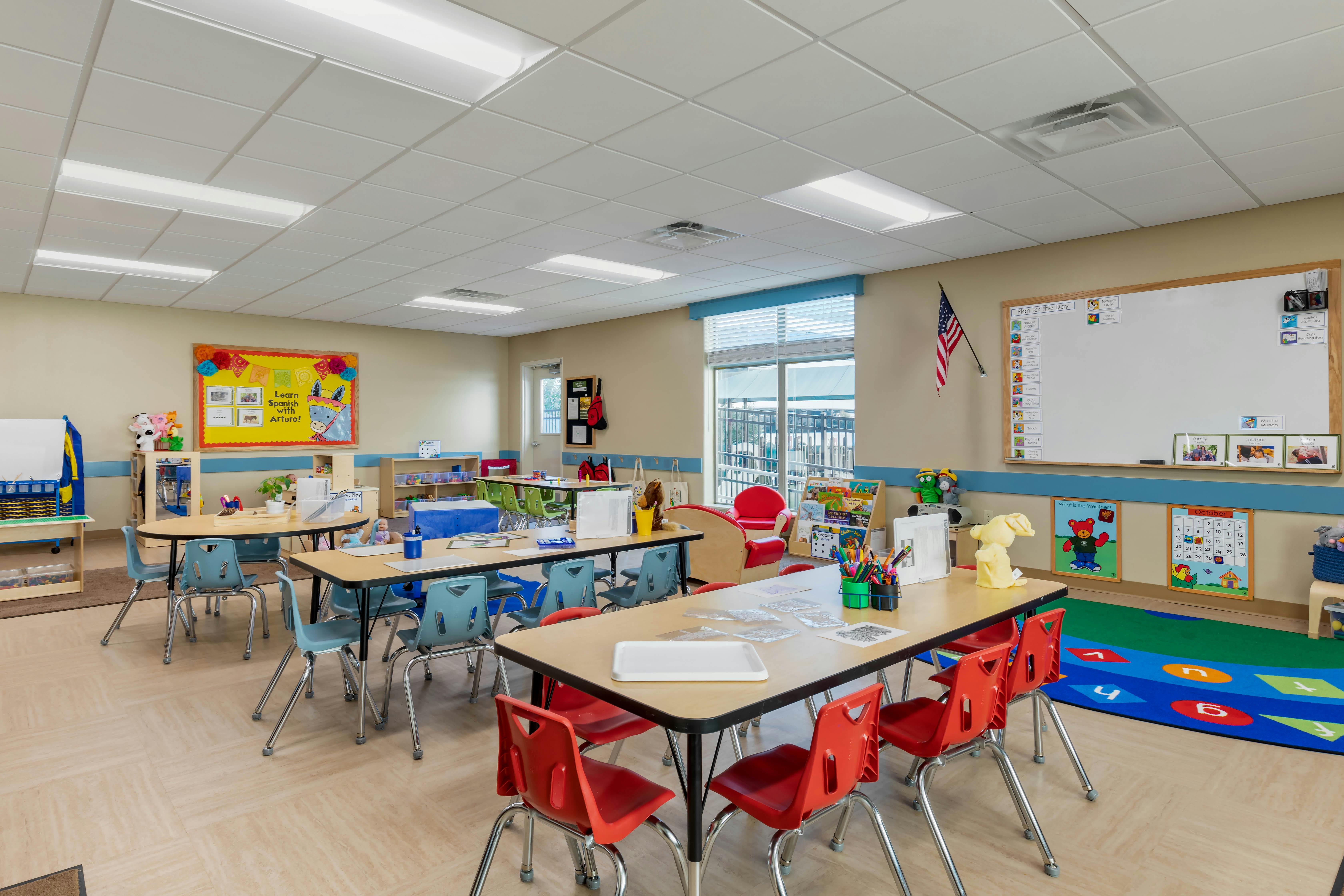 Classroom with child-sized tables and chairs, a whiteboard, and a Spanish learning poster