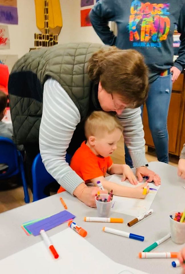 Person helping a child draw with markers at a table