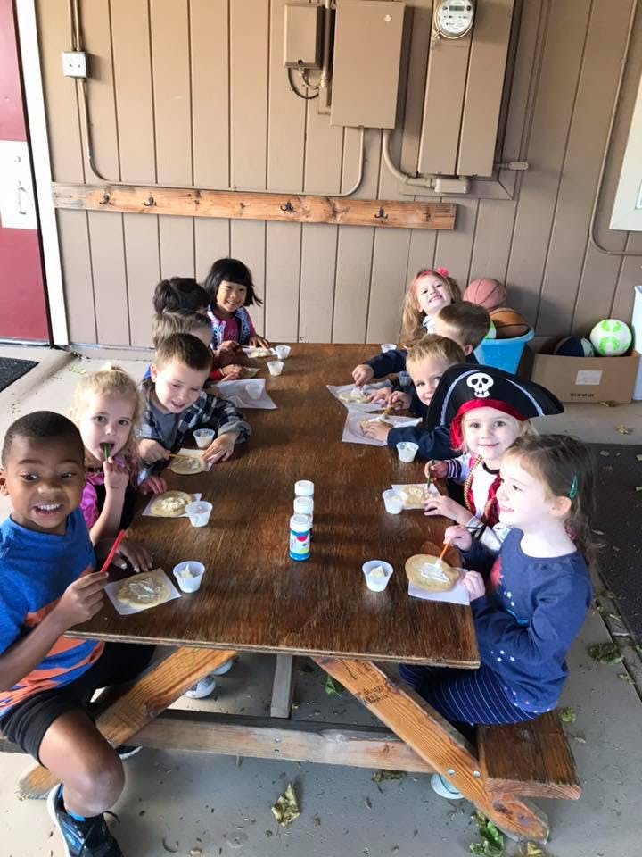 Children sitting at a picnic table with crafts