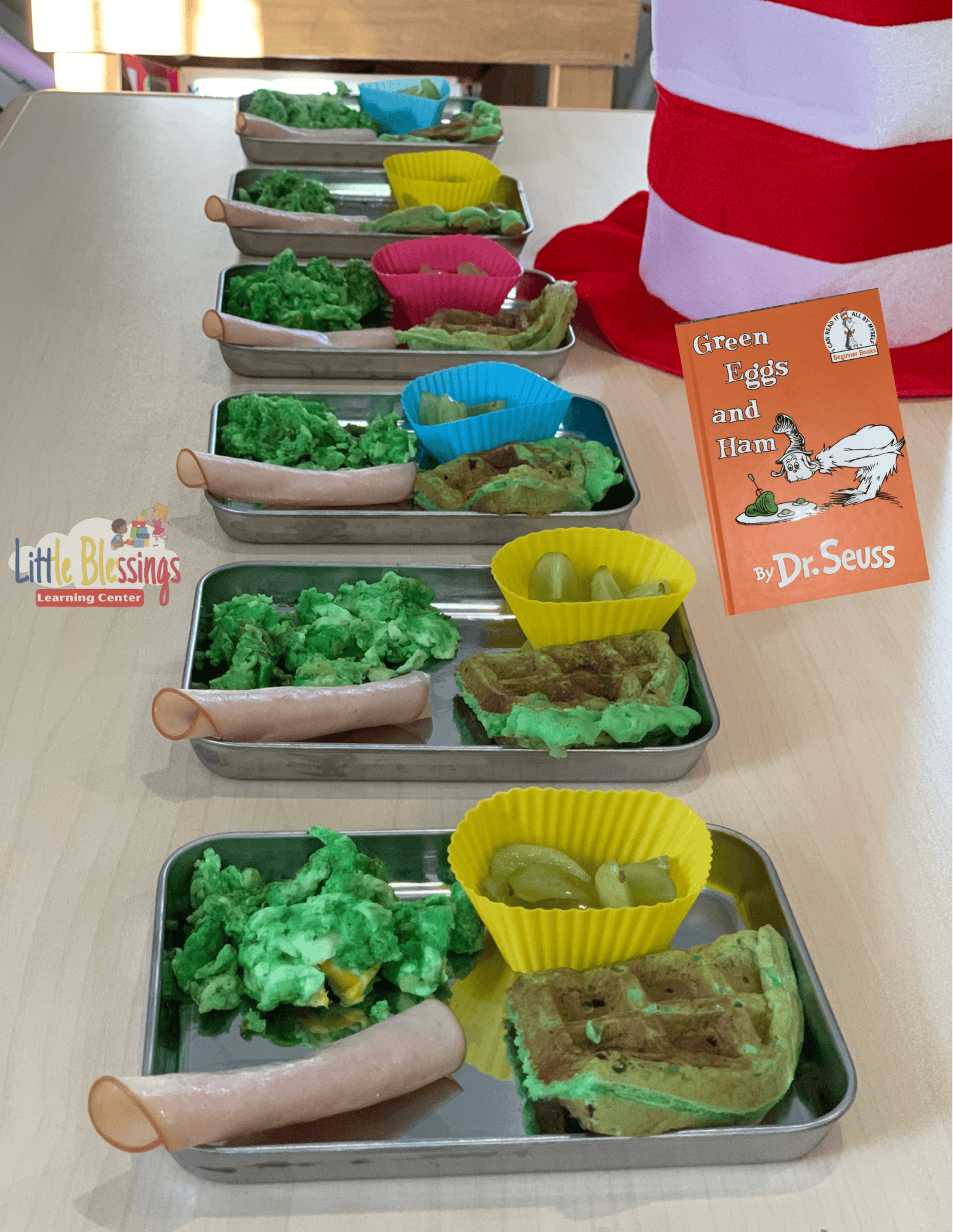 Trays of green eggs, ham, and waffles with a "Green Eggs and Ham" book