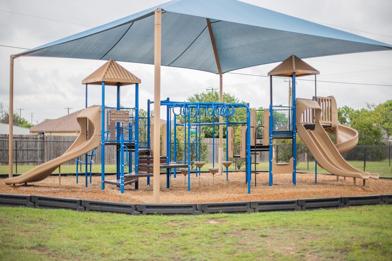 Playground structure with slides and monkey bars under a large shade canopy