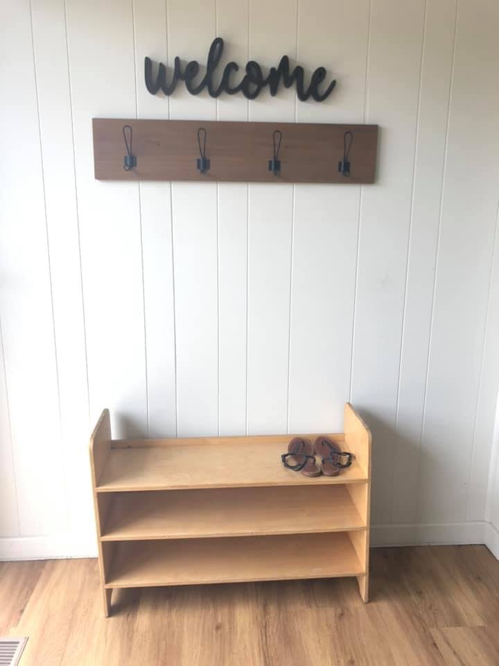 Shoe rack with sandals and a coat rack with a welcome sign above