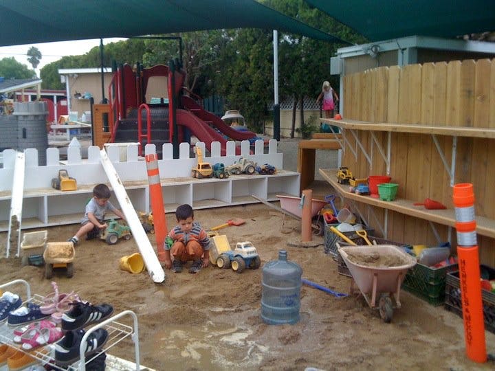 Two children playing in a sandbox with toy trucks