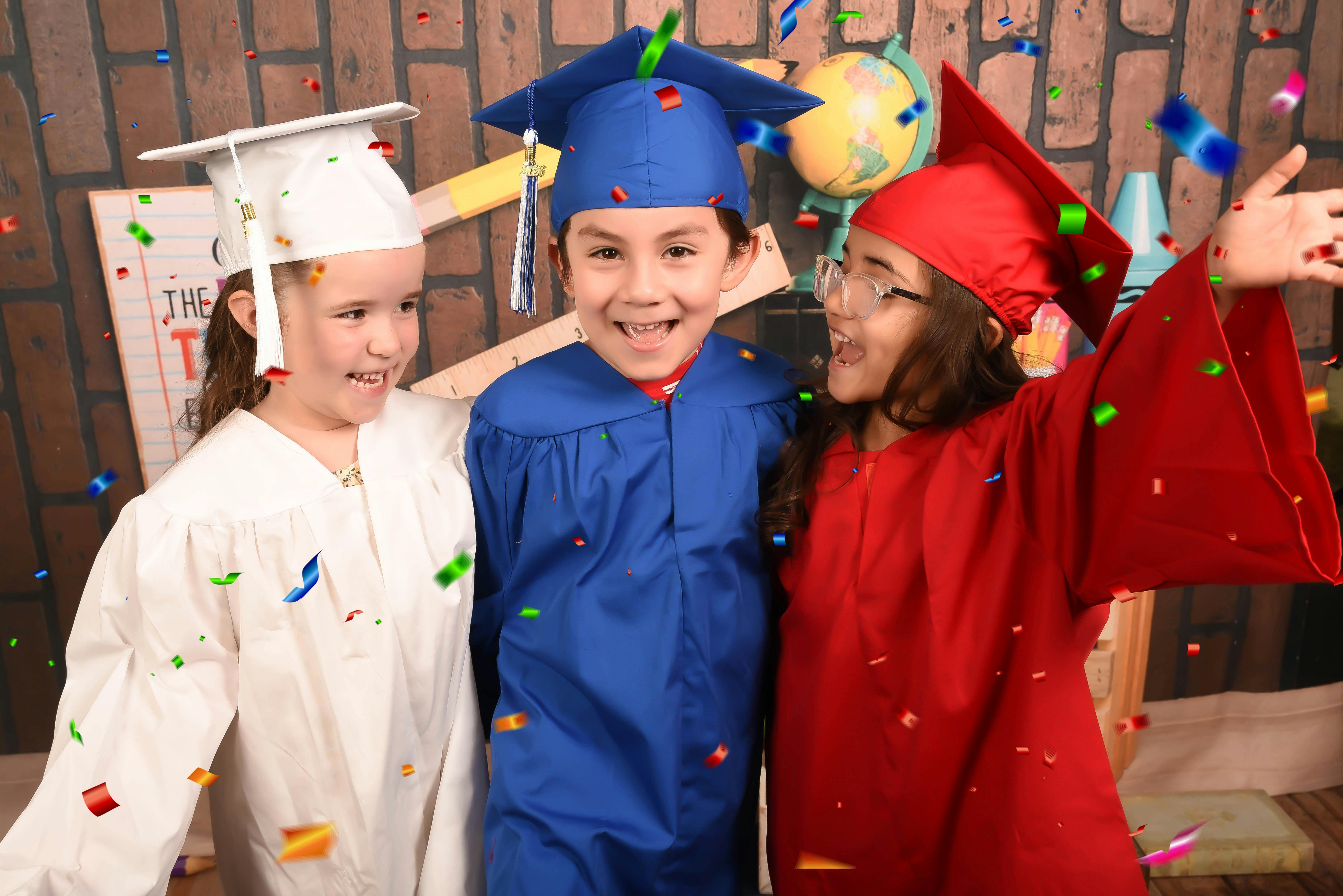 Three children in graduation caps and gowns celebrating with confetti