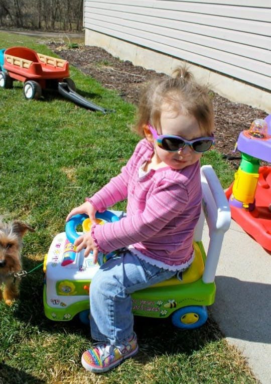 Child wearing sunglasses sitting on a ride-on toy outdoors