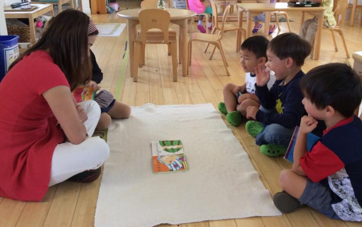 Person and three children sitting on floor looking at a book