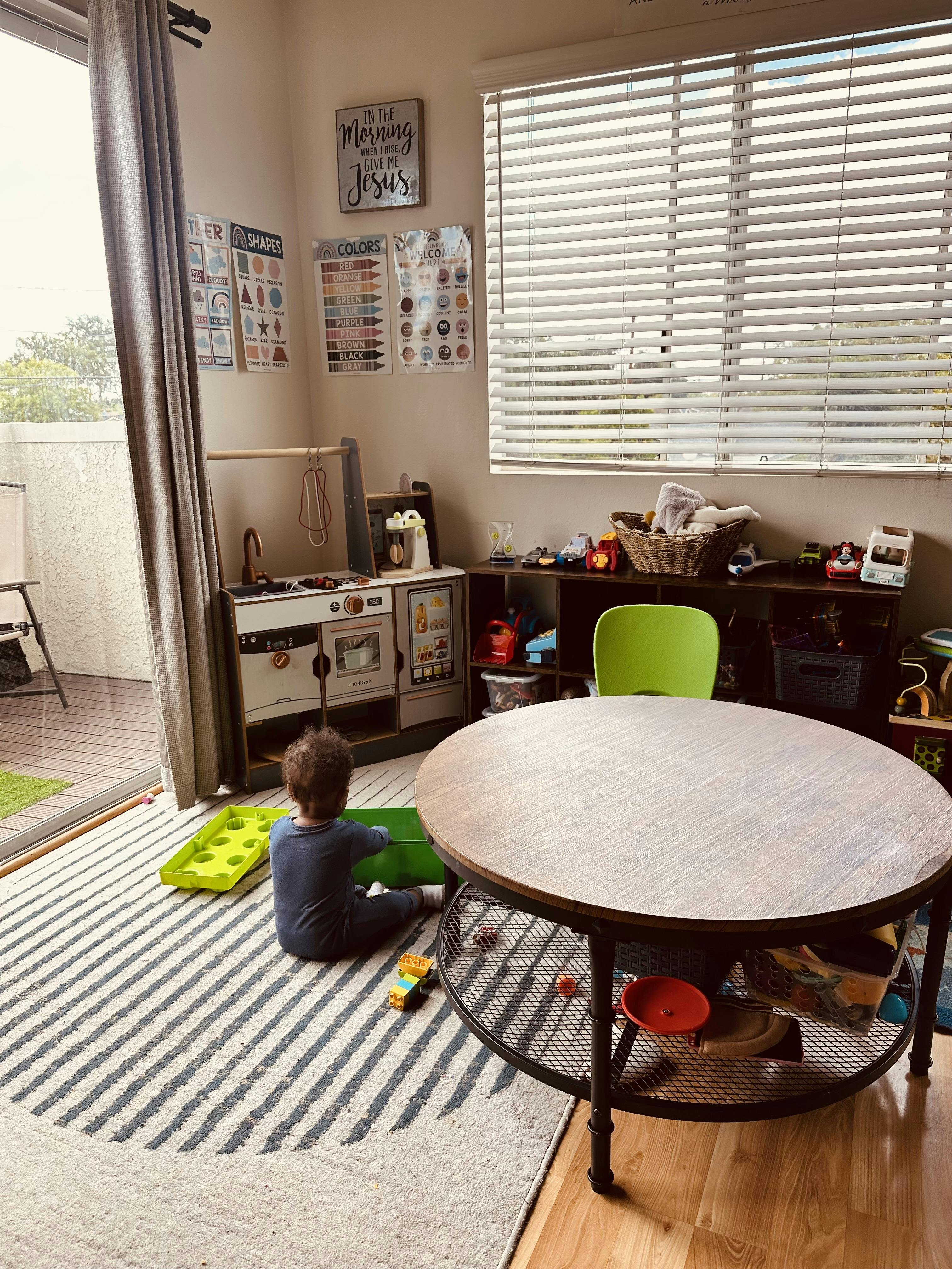 Child playing with toys on a rug next to a toy kitchen set