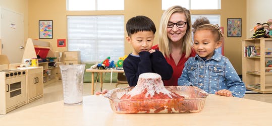 Adult and two children watching a volcano science experiment in a classroom