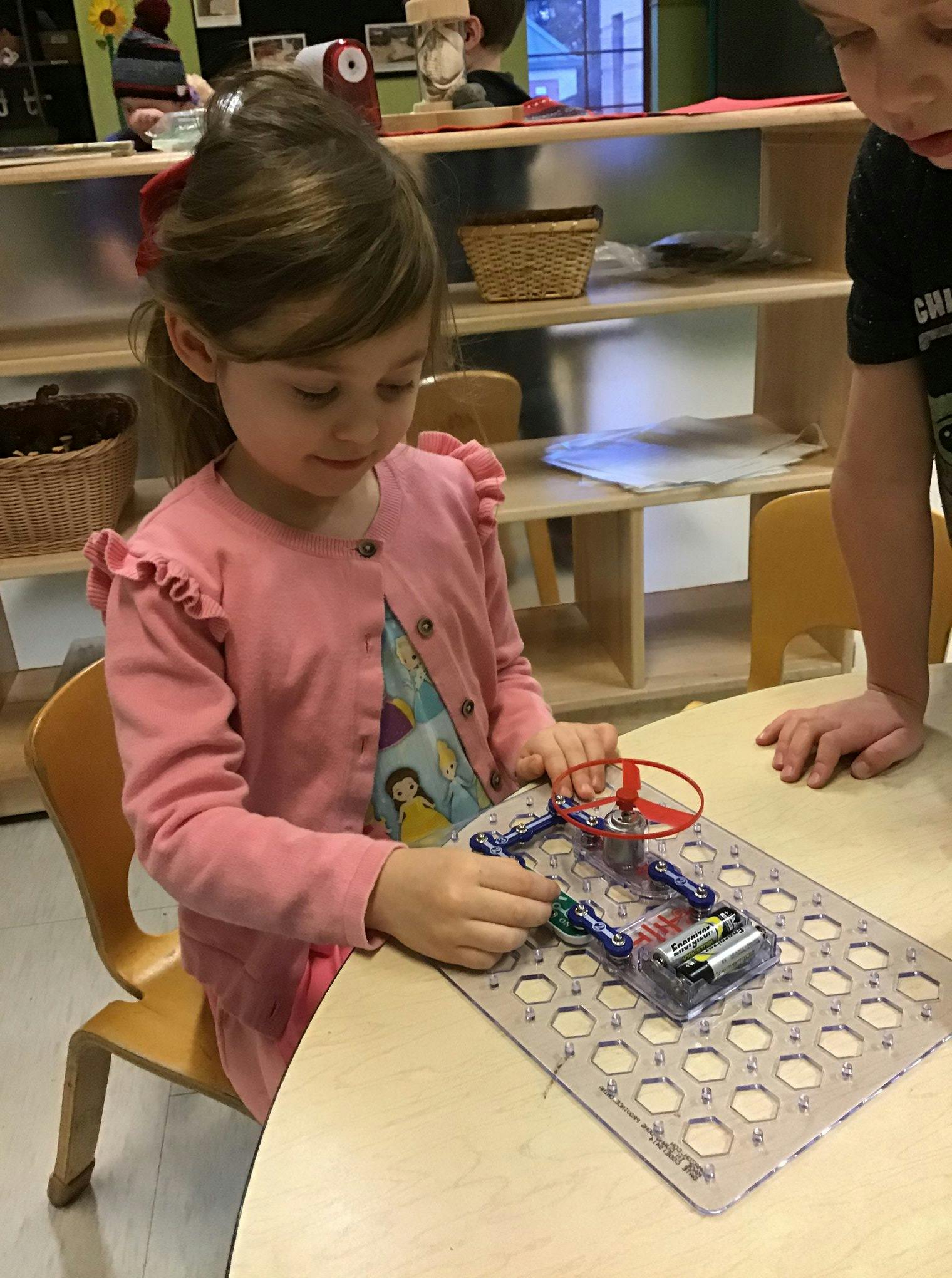 Child assembling a circuit board with batteries and a small fan