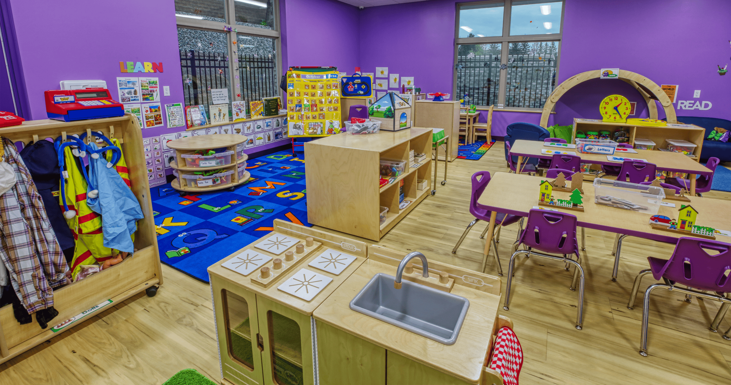 A purple classroom with a play kitchen, tables, and a dress-up rack