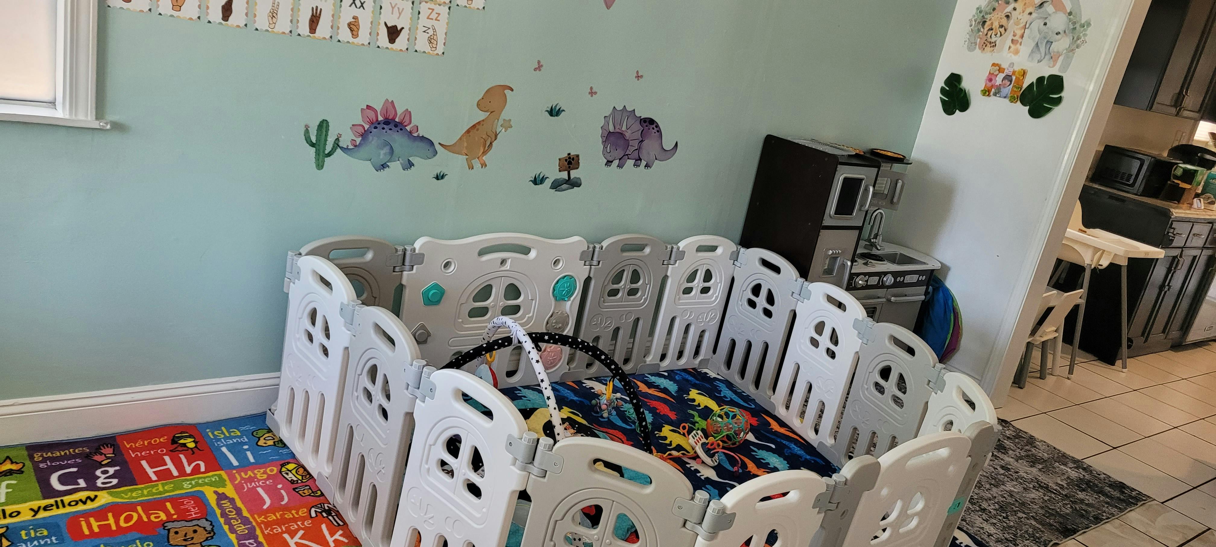 Playpen with a colorful mat inside, dinosaur wall decals