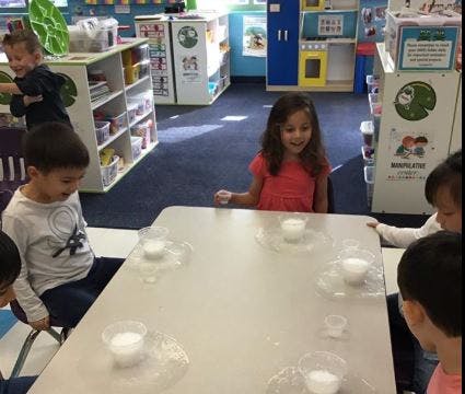 Children at a table with cups and white powder in a classroom