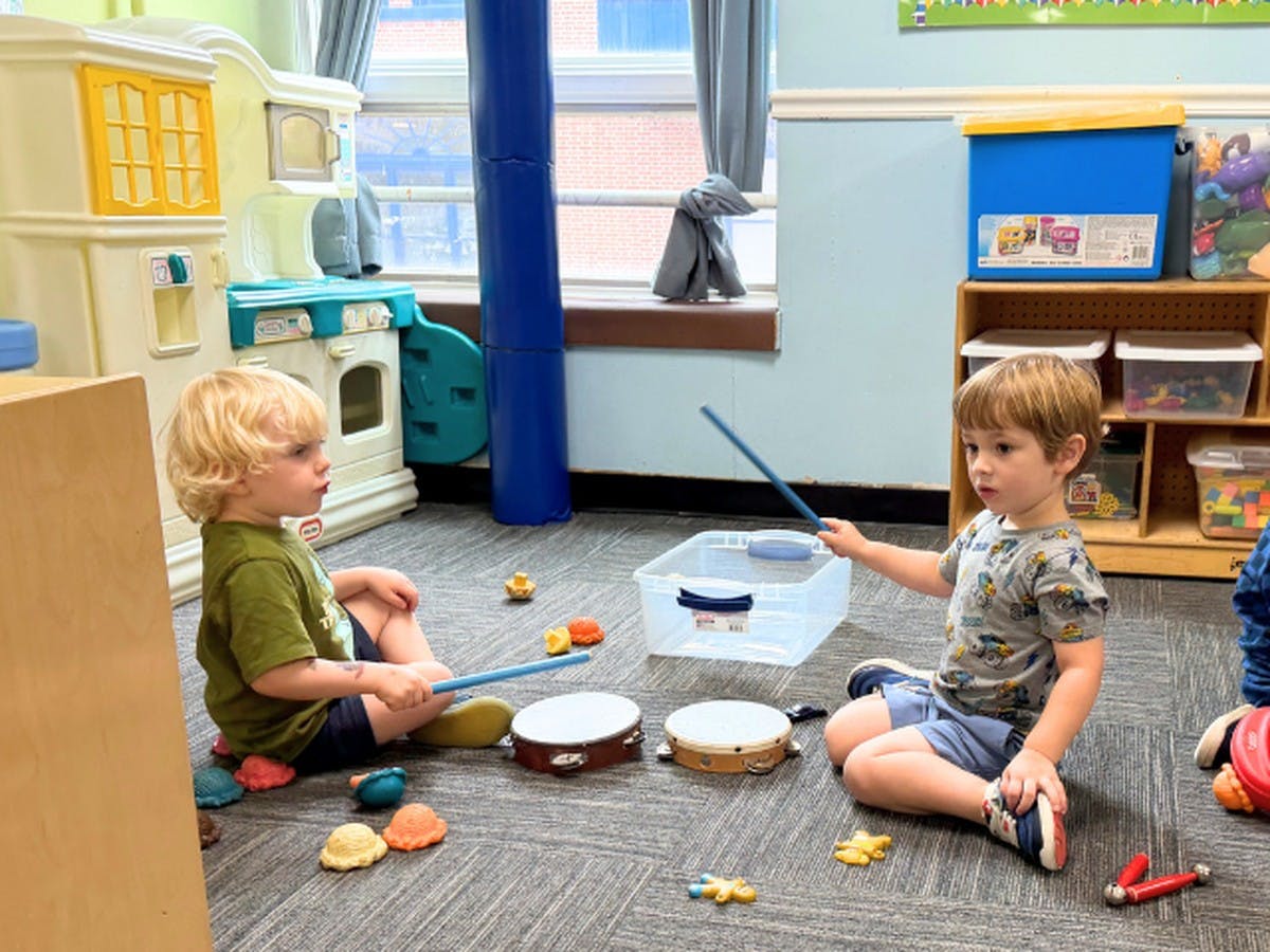 Two children sitting on the floor in a classroom playing with toy drums
