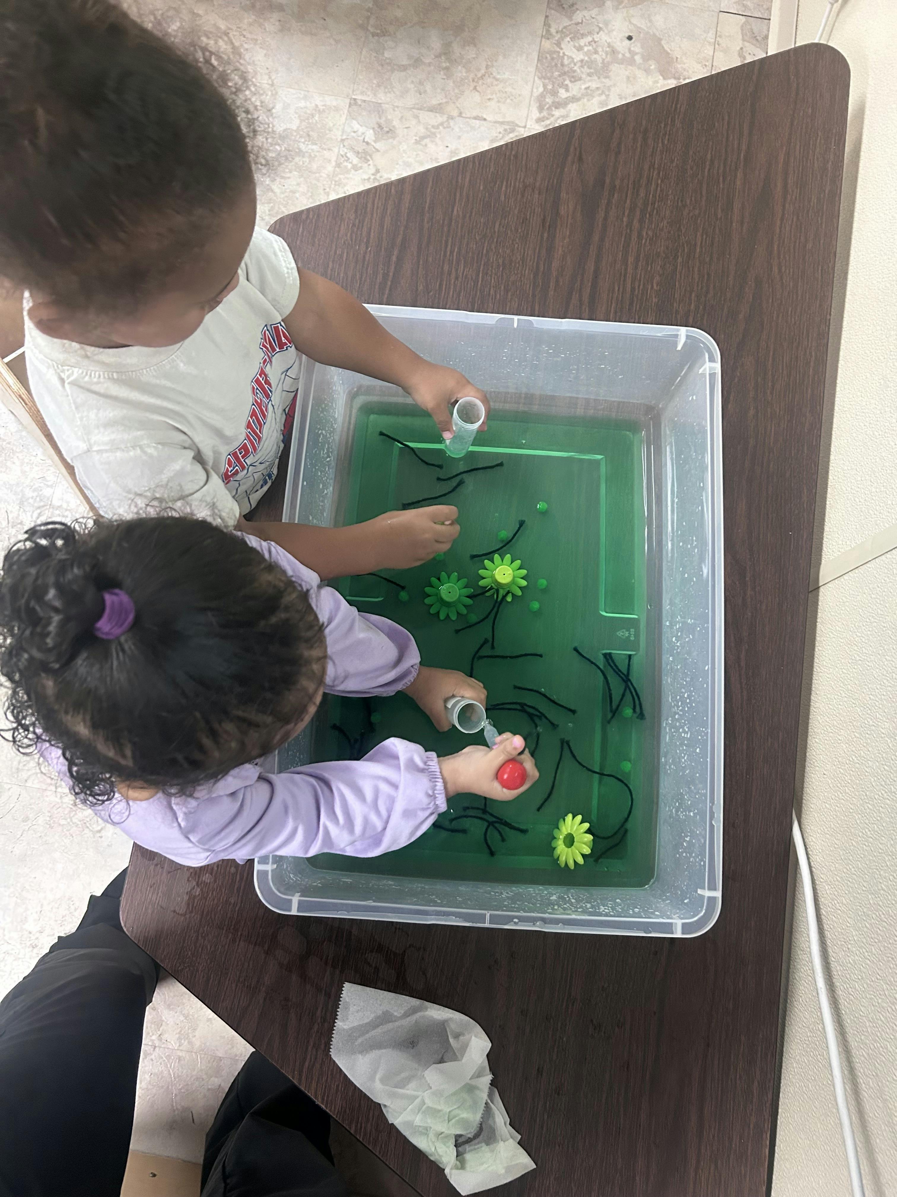 Two children playing with water and toys in a clear bin