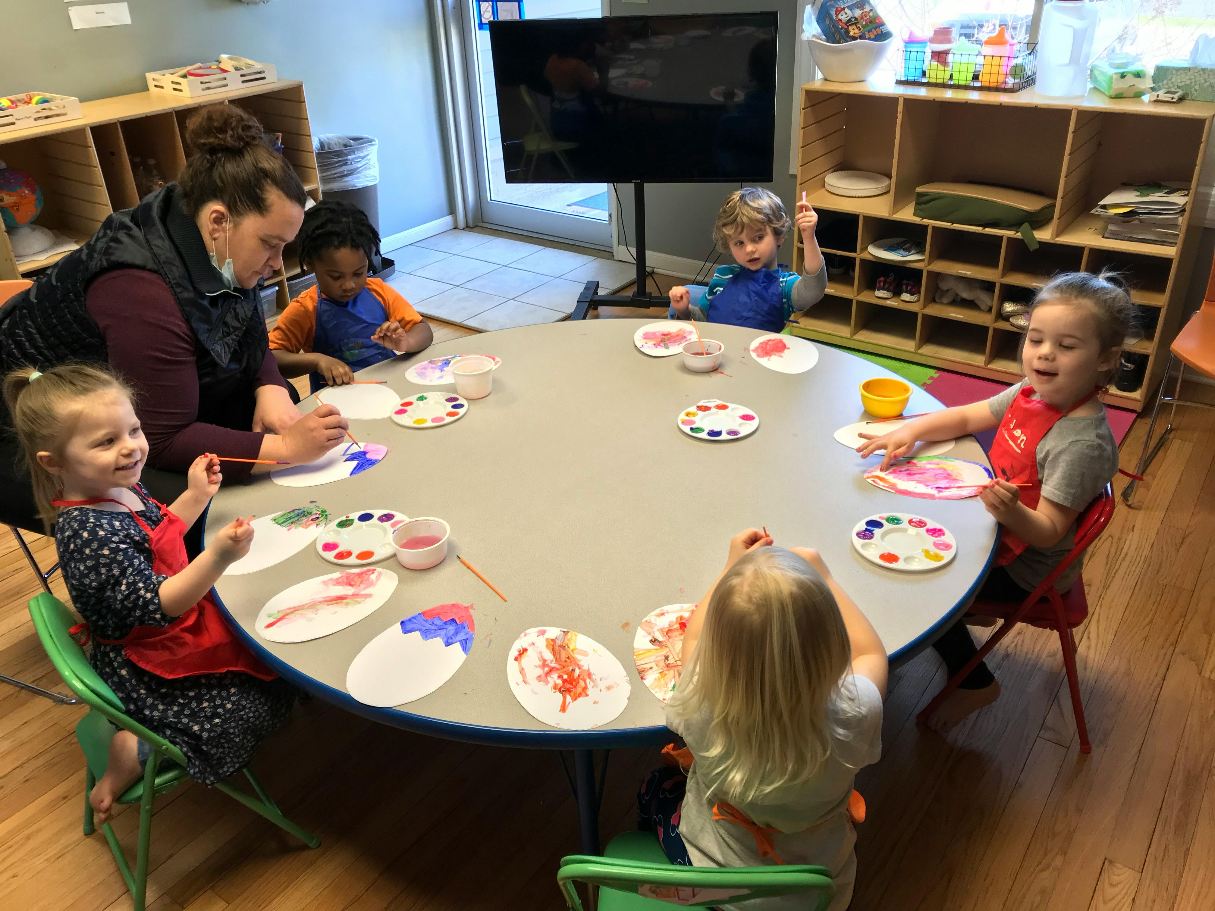 Adult and children painting at a round table in a classroom