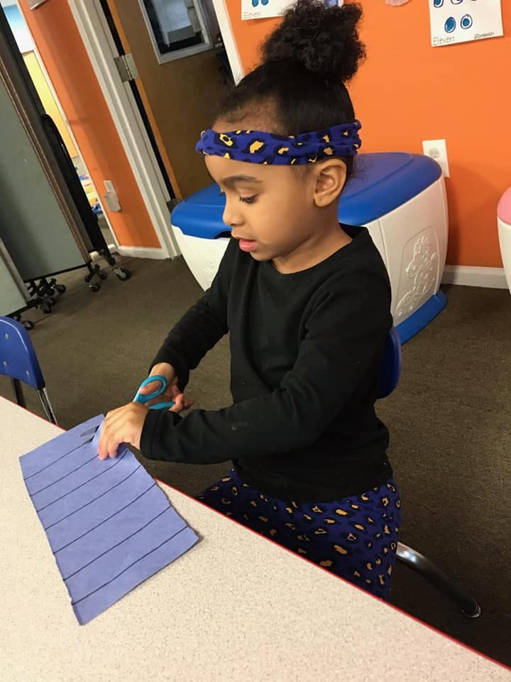 Child cutting paper with scissors at a table