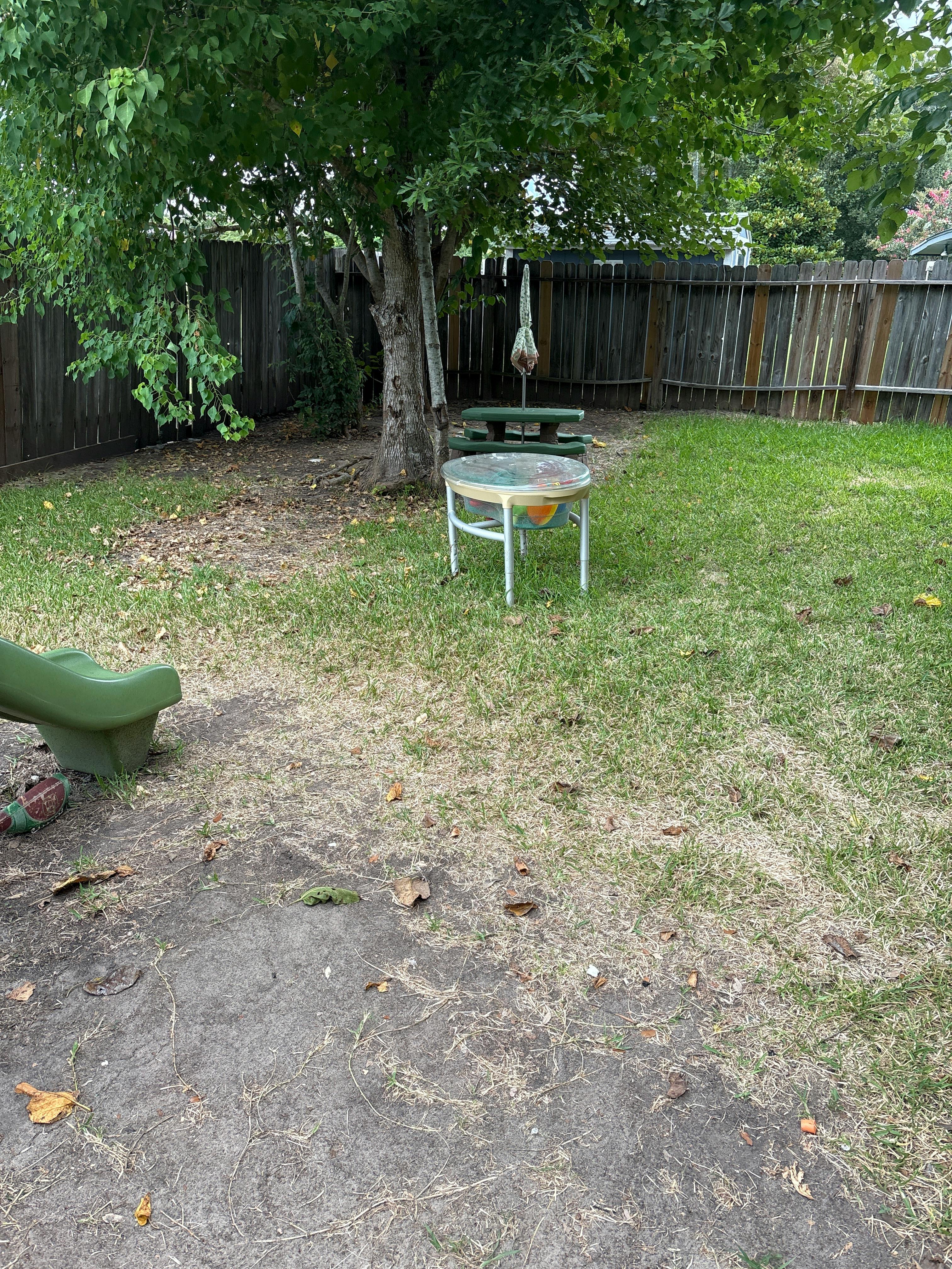 Small patio table and child slide in a backyard with a wooden fence