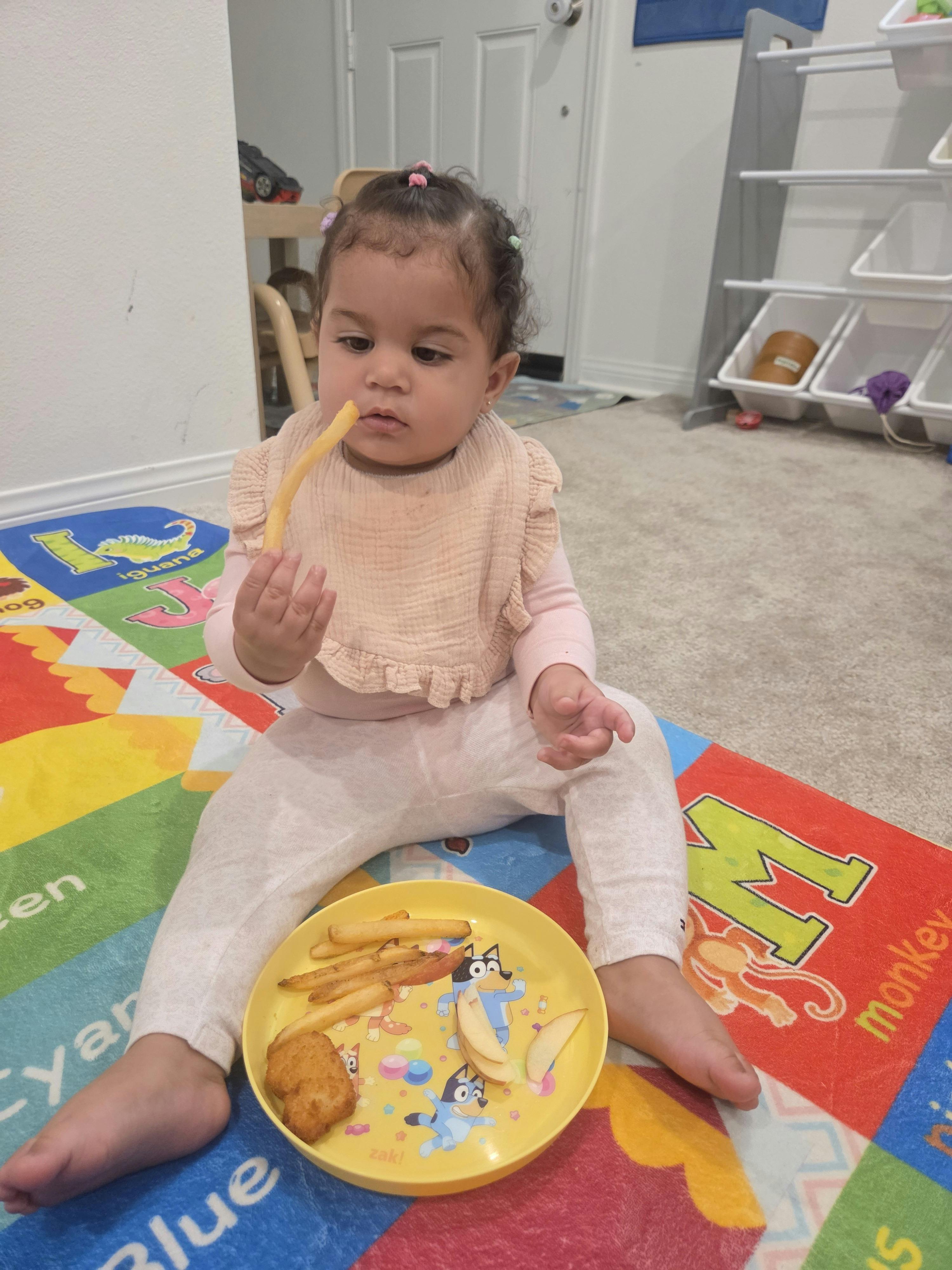 Child eating a french fry while sitting on a colorful play mat