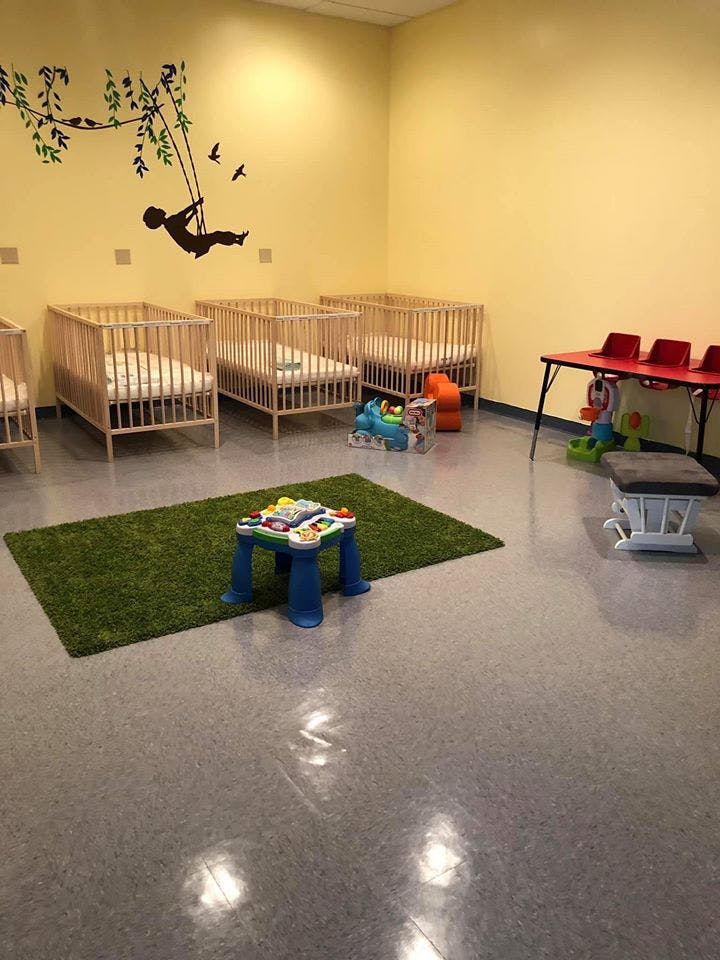 Nursery room with multiple cribs, a play mat, and a small table