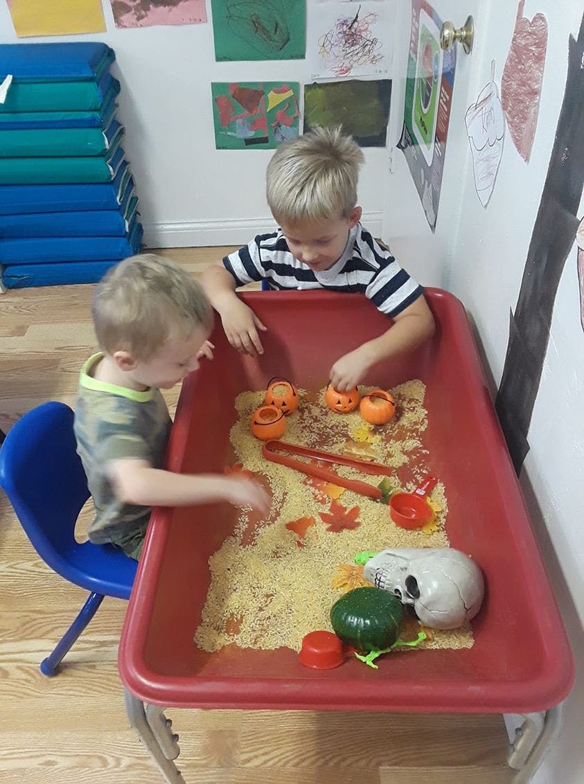 Two children playing with sensory bin filled with pasta and small toys