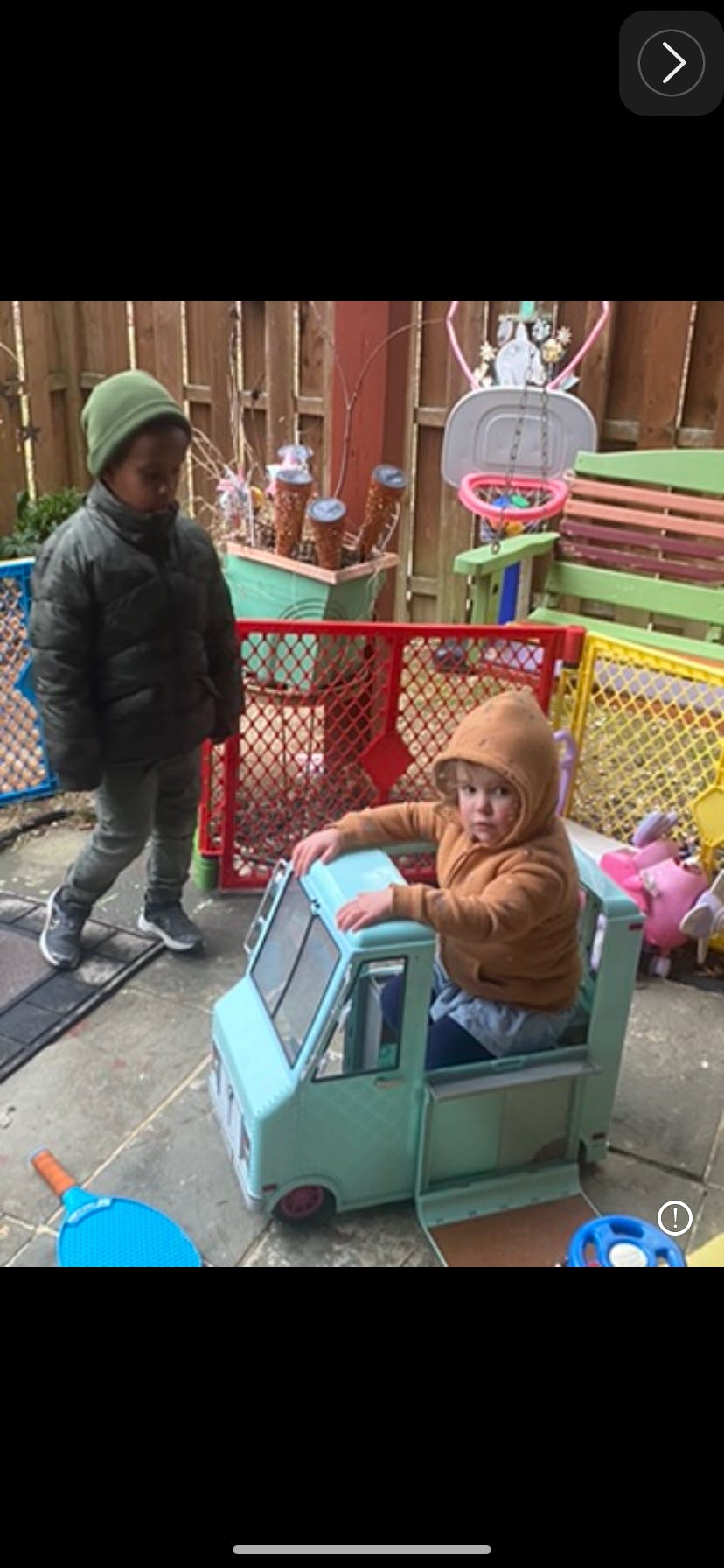 Child in a toy truck and another child standing nearby