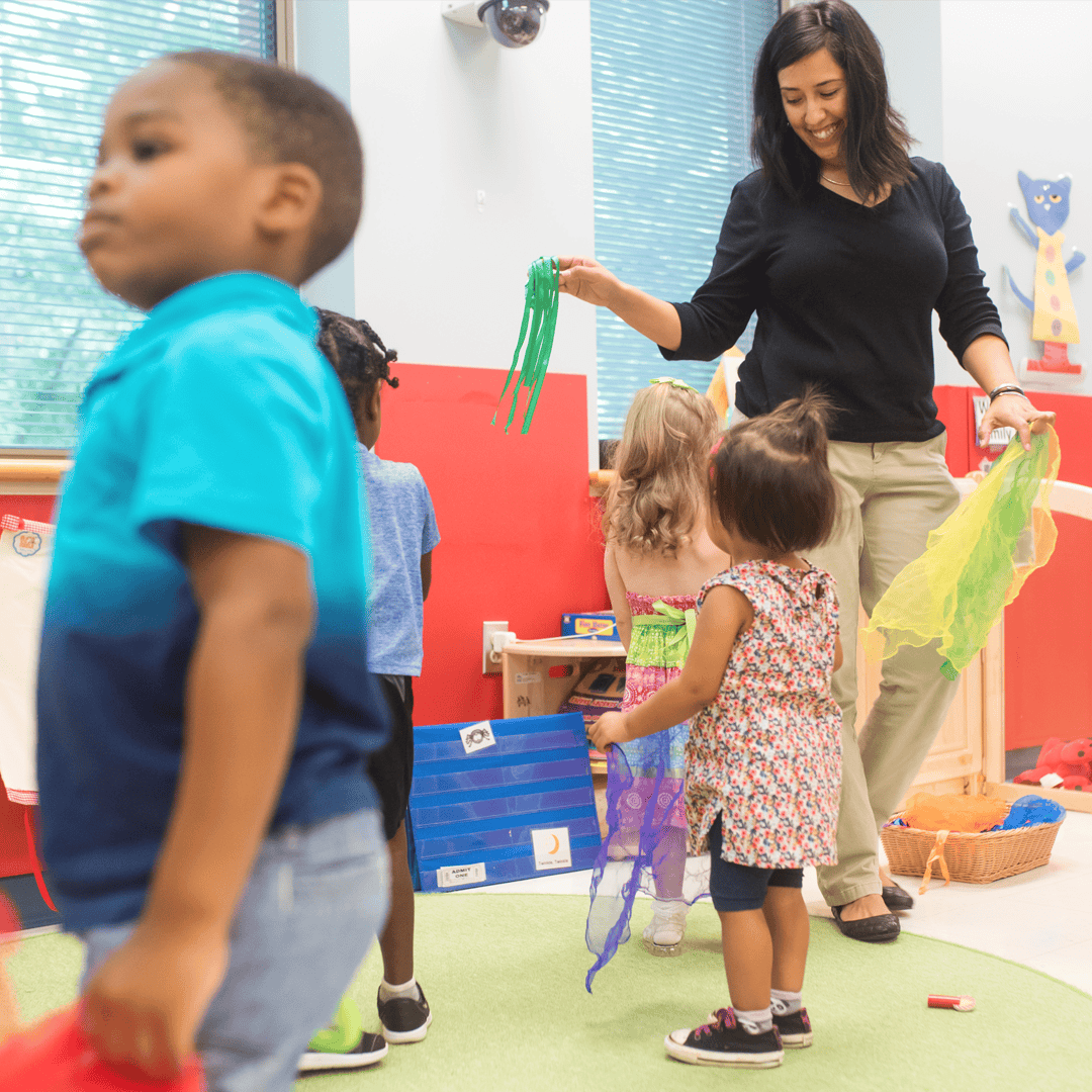 Adult and children in a classroom holding colorful scarves
