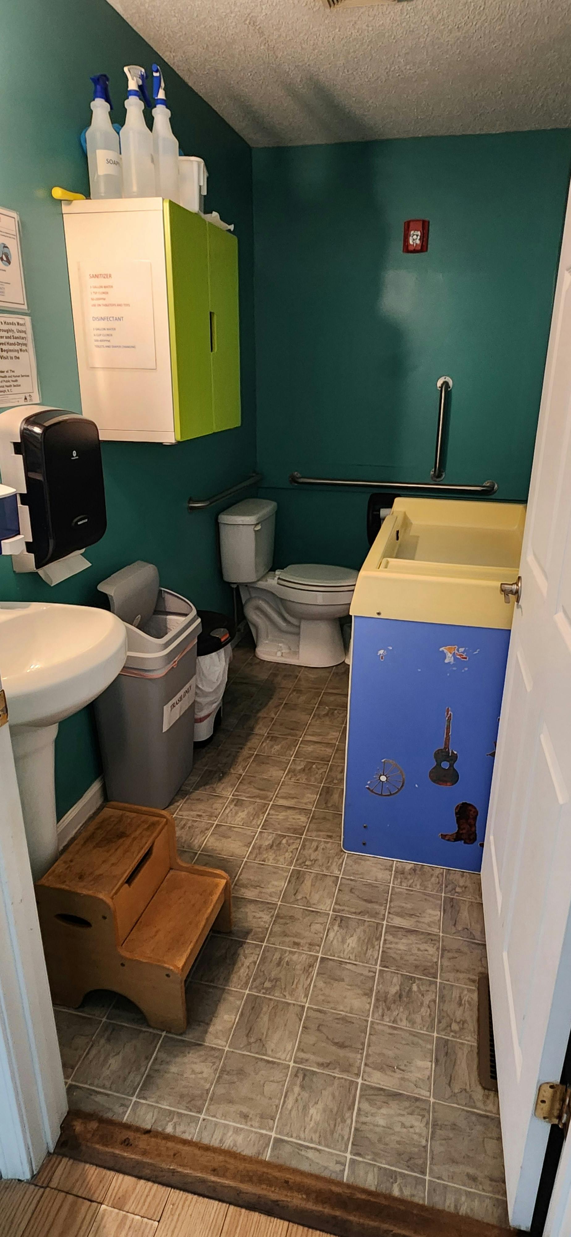 Bathroom with toilet, sink, changing station, and step stool