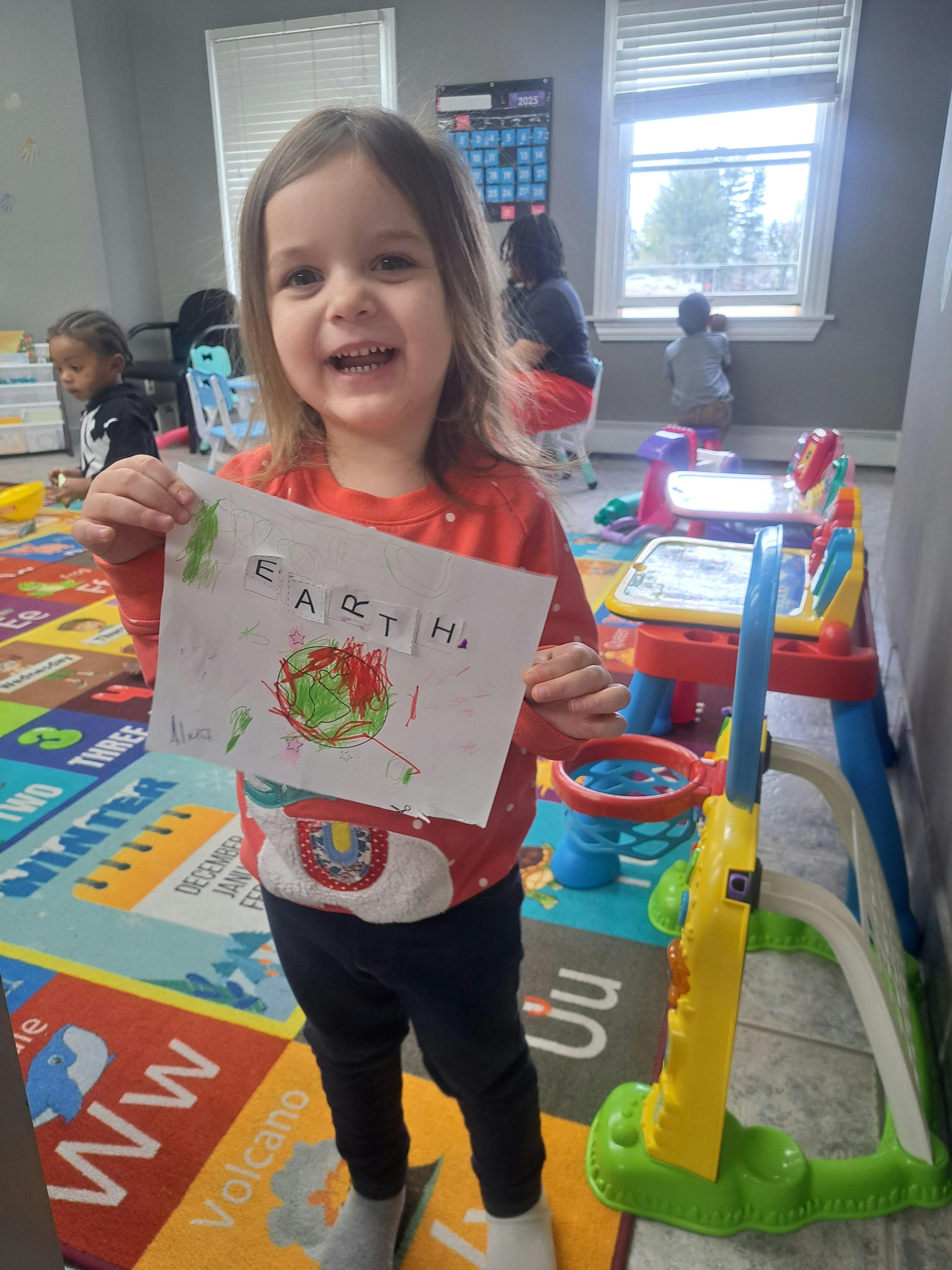 Child holding up a drawing of the Earth with the word "EARTH" written above it