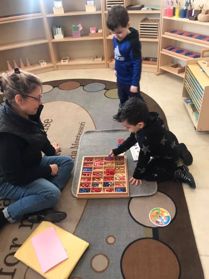 Adult and two children on a rug with a wooden letter tray